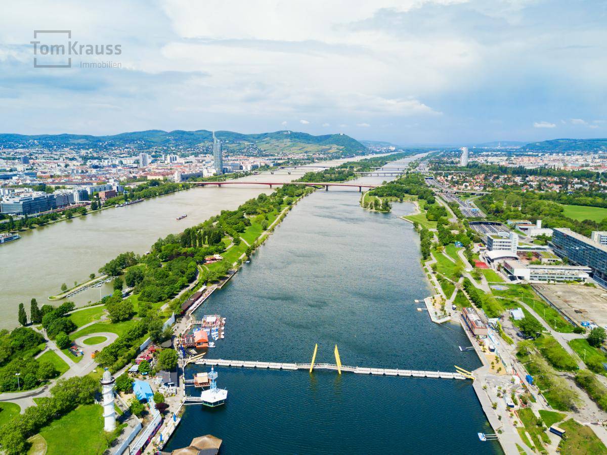 Weitläufige Luftaufnahme einer Stadtlandschaft mit Fluss, Brücken und grünen Uferbereichen.