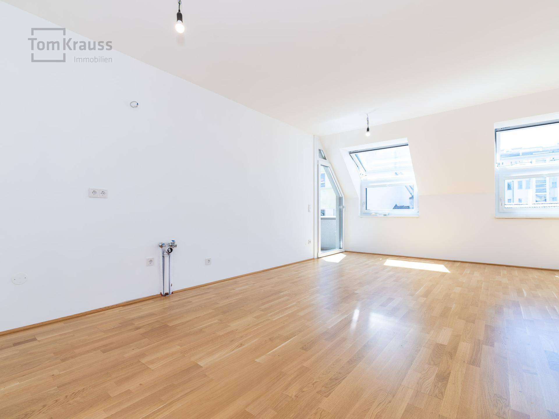 Leerer Wohnbereich mit Holzparkett, Dachfenstern und Vorbereitung für eine Küche.