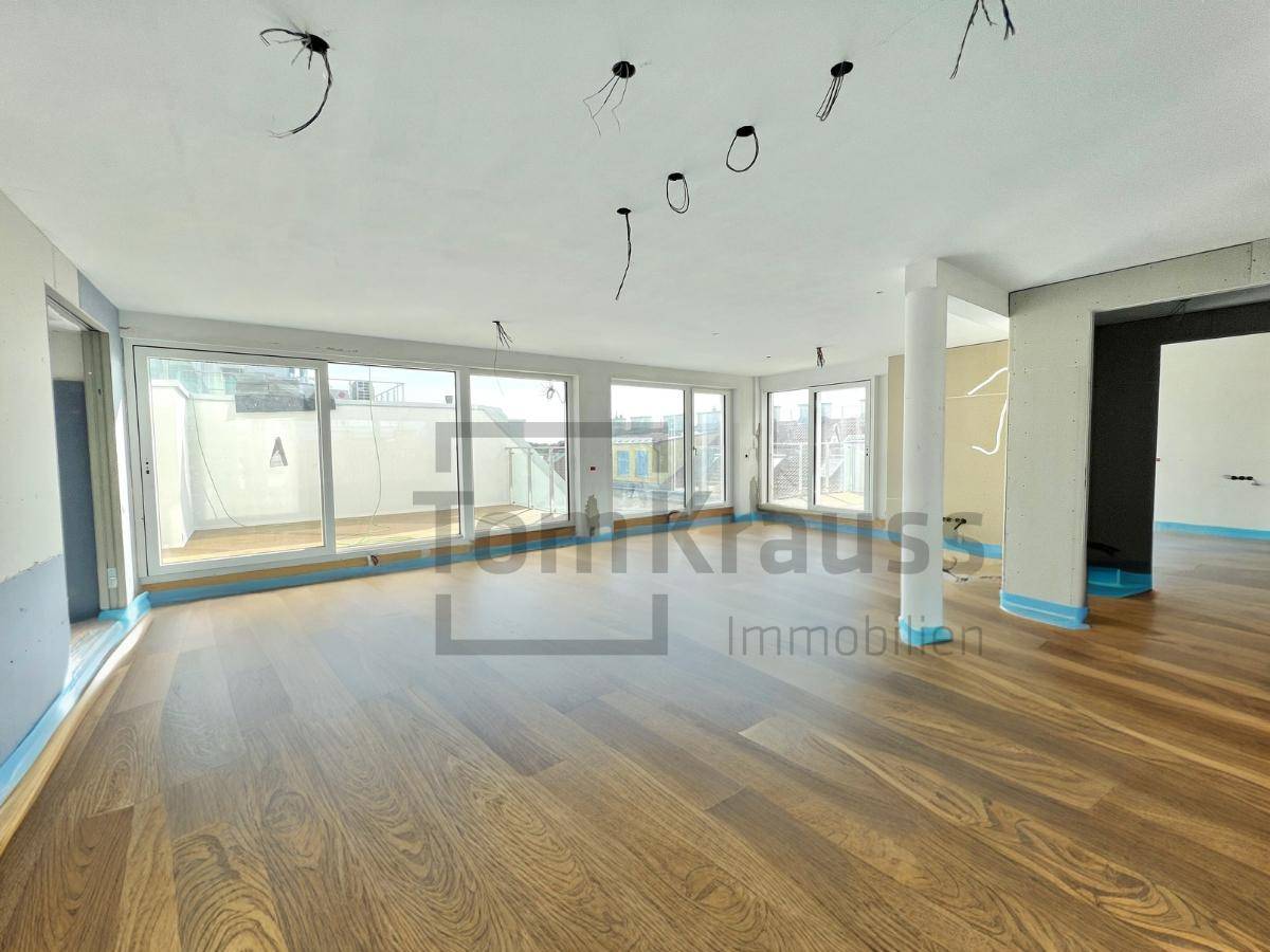 Geräumiger Wohnbereich im Rohbau mit großen Fensterfronten und hochwertigem Holzboden.