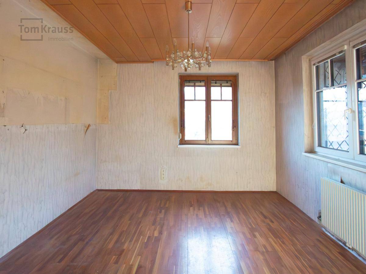 Leeres Zimmer mit Parkettboden, Holzdecke und zwei Fenstern, bereit für eine Renovierung.