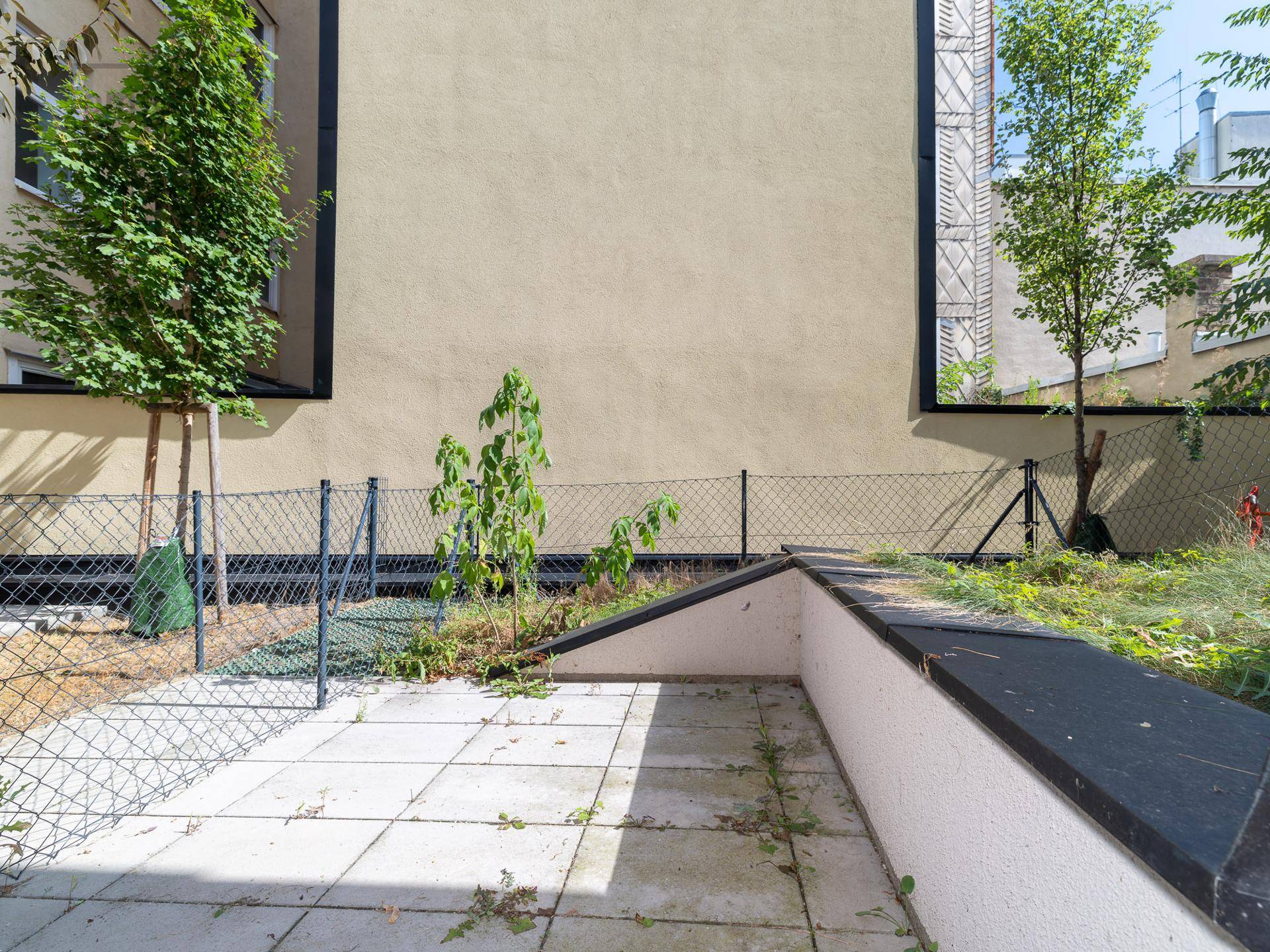 Unmöblierte Terrasse mit Fliesenboden und angrenzender Grünfläche, bereit zur Gestaltung.