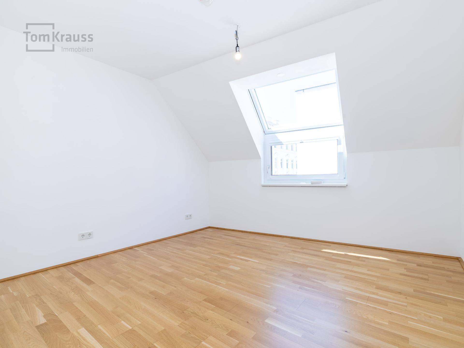 Leeres Schlafzimmer im Dachgeschoss mit Holzparkettboden und einem großen Dachfenster.