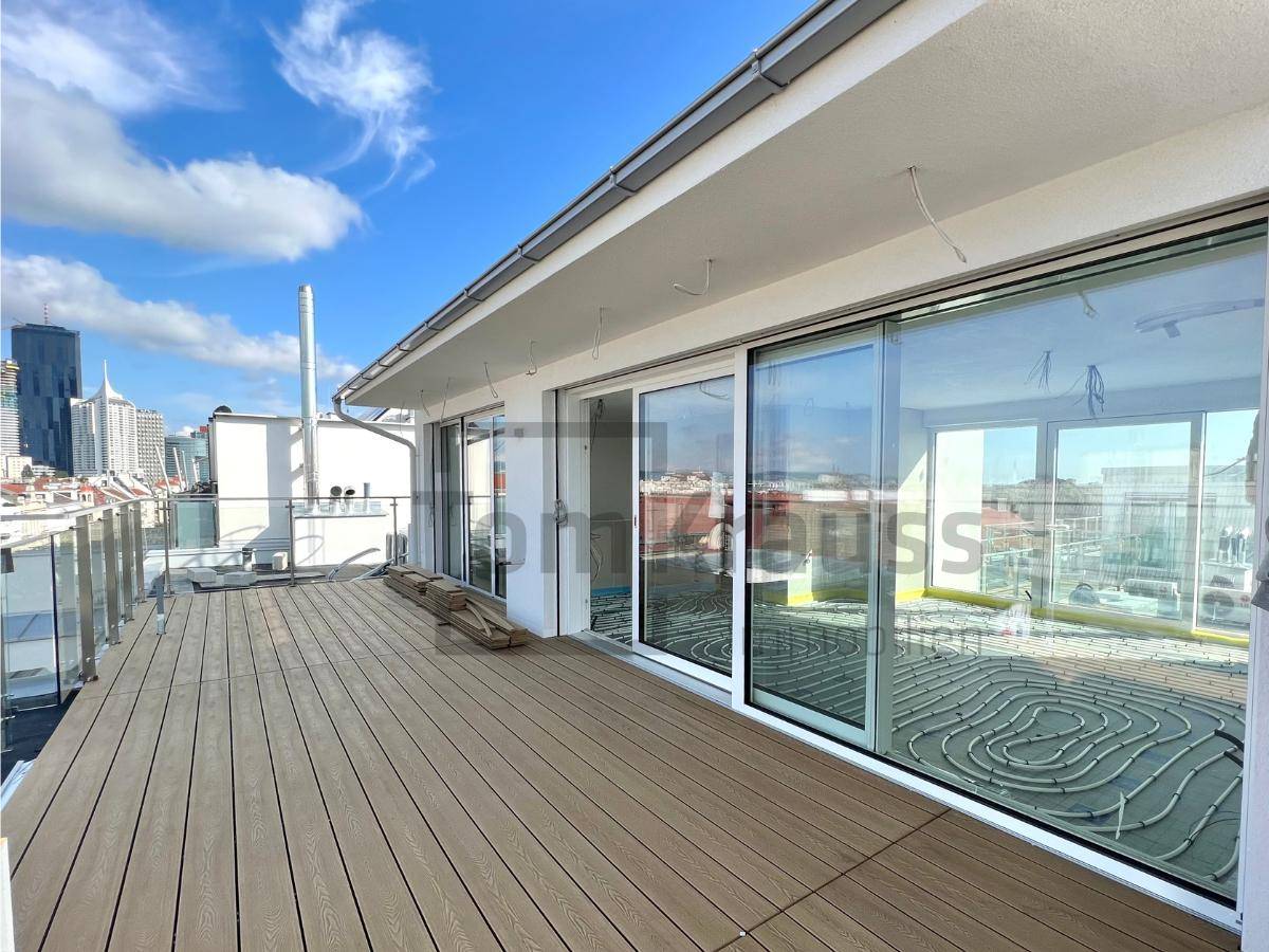 Dachterrasse im Bau mit sichtbaren Fußbodenheizungsrohren und Blick auf die Stadt.
