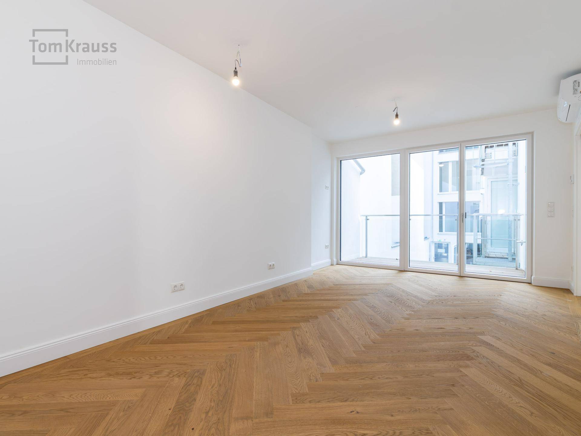 Geräumiges Wohnzimmer mit Fischgrätparkett und großen Schiebetüren zum Balkon.