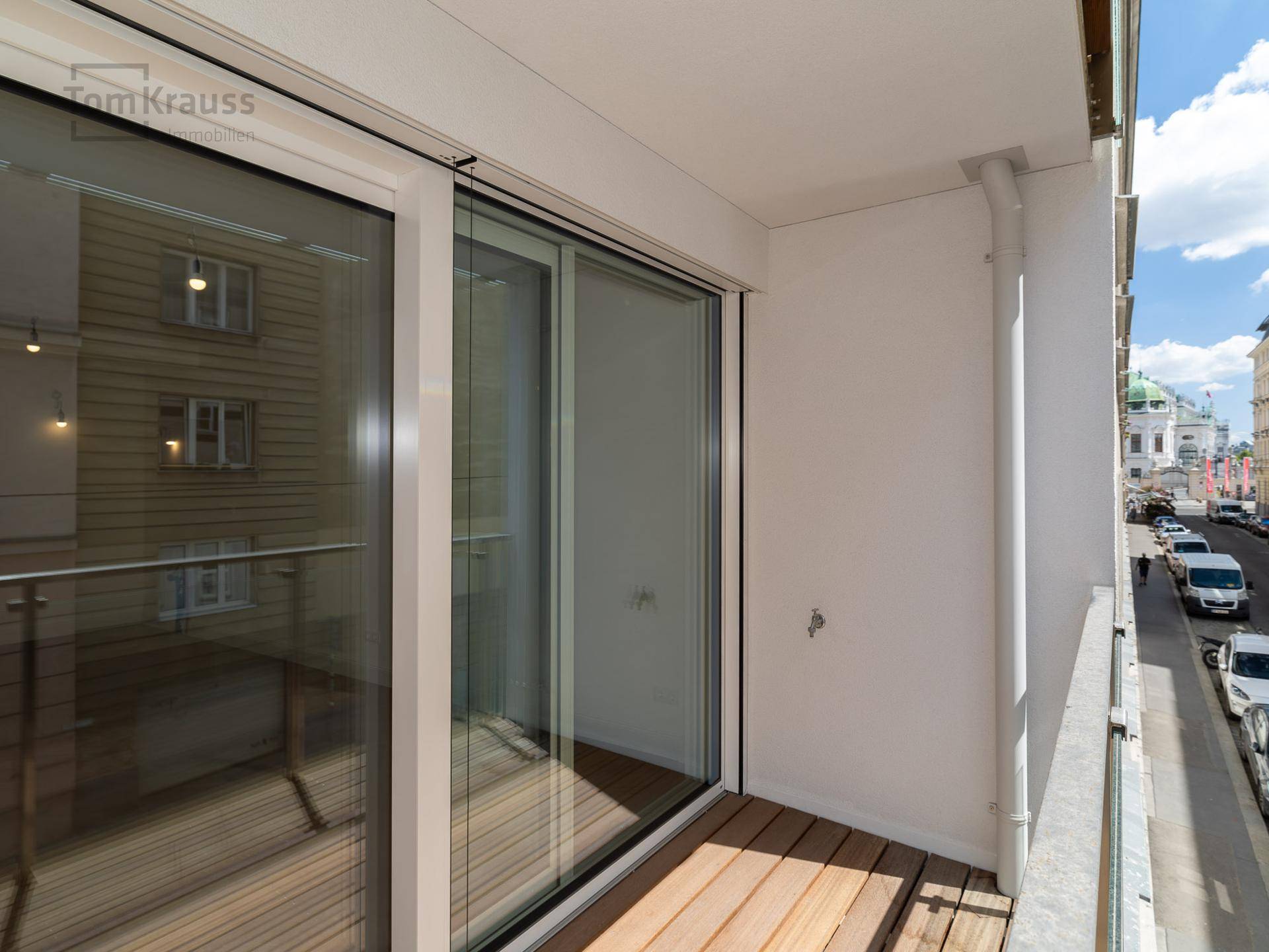 Kleiner Balkon mit Holzboden und Blick auf die belebte Stadtstraße.