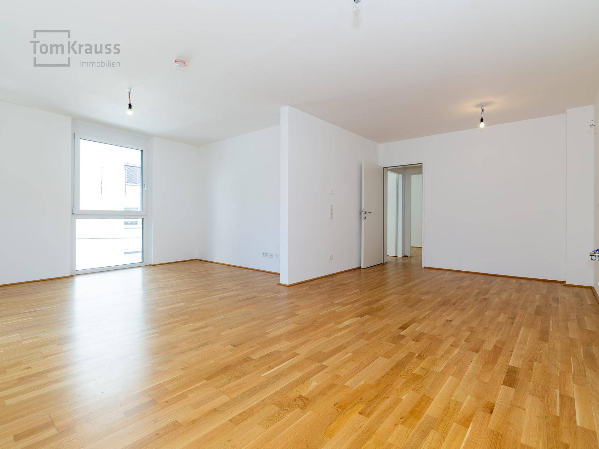 Heller, leerer Raum mit Parkettboden und großem Fenster, bereit zur individuellen Gestaltung.