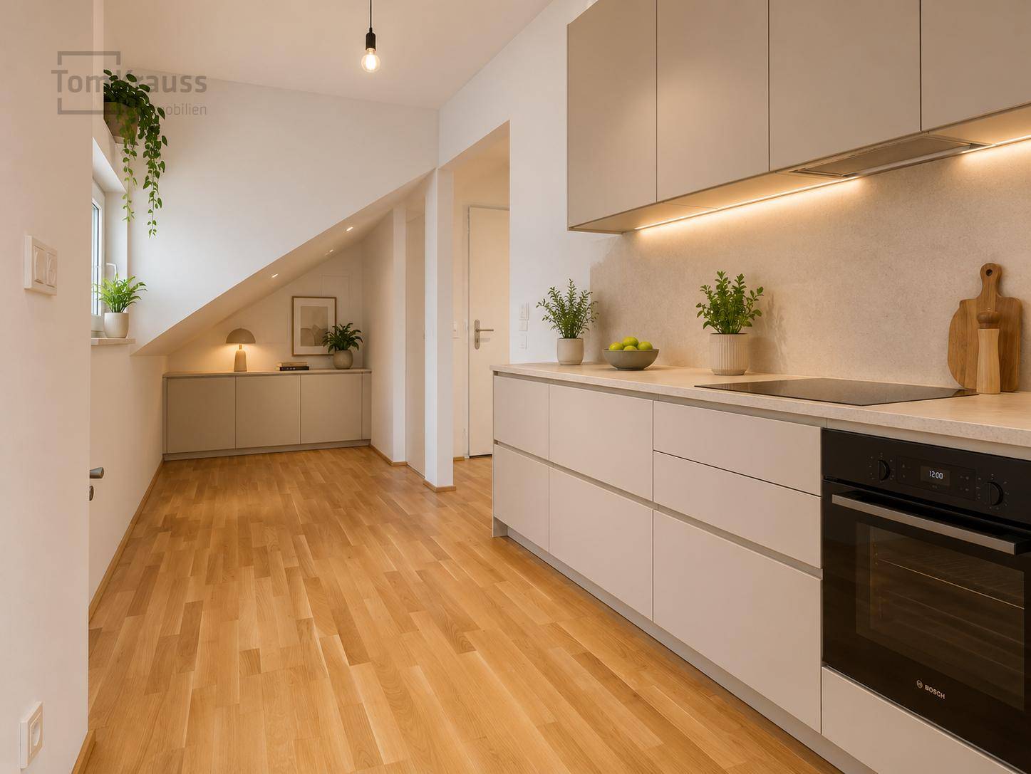 Moderne Küche mit hellgrauen Schränken, integriertem Backofen und Holzboden unter Dachschräge.