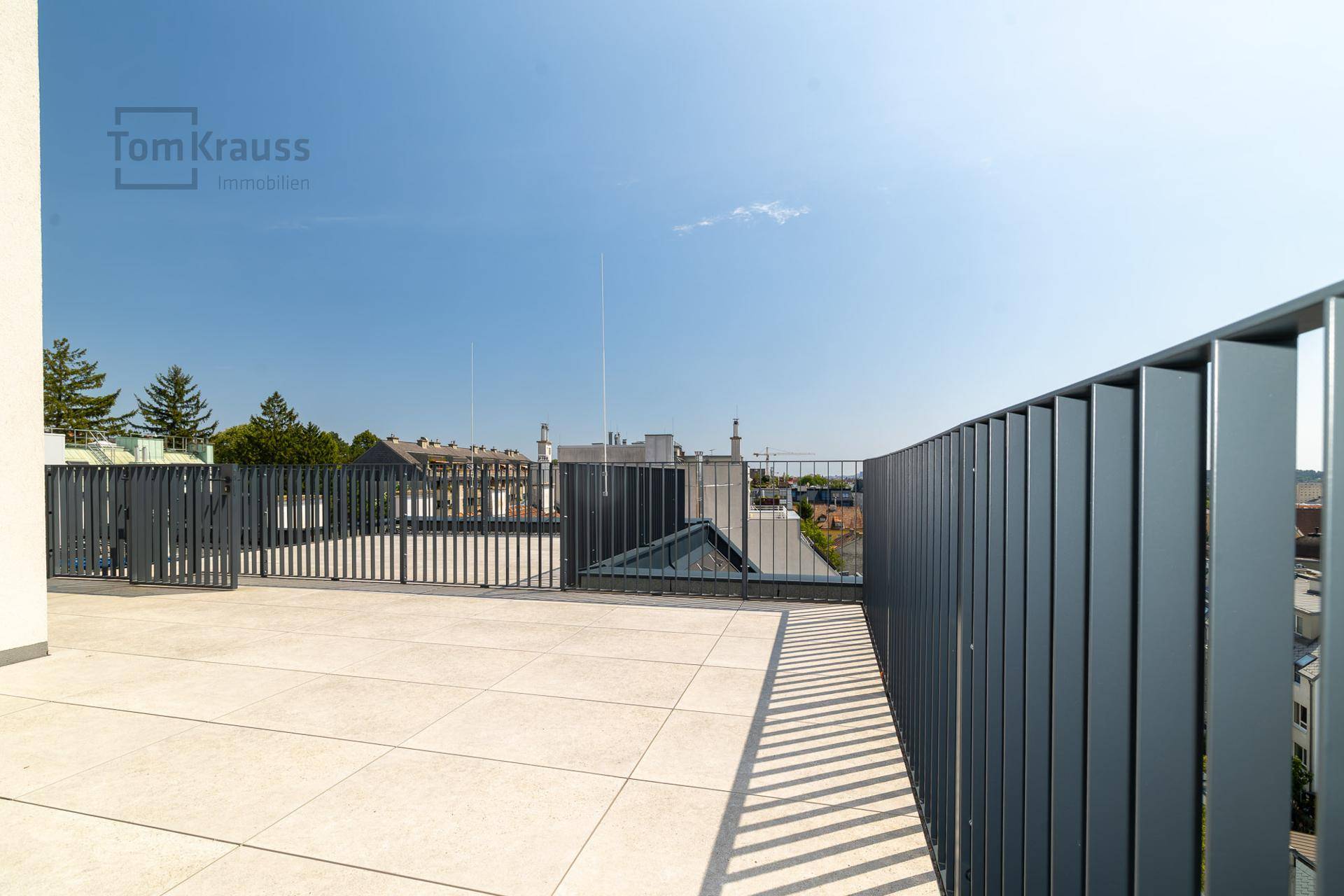 Weitläufige Dachterrasse mit hellem Fliesenboden und moderner Brüstung unter klarem Himmel.