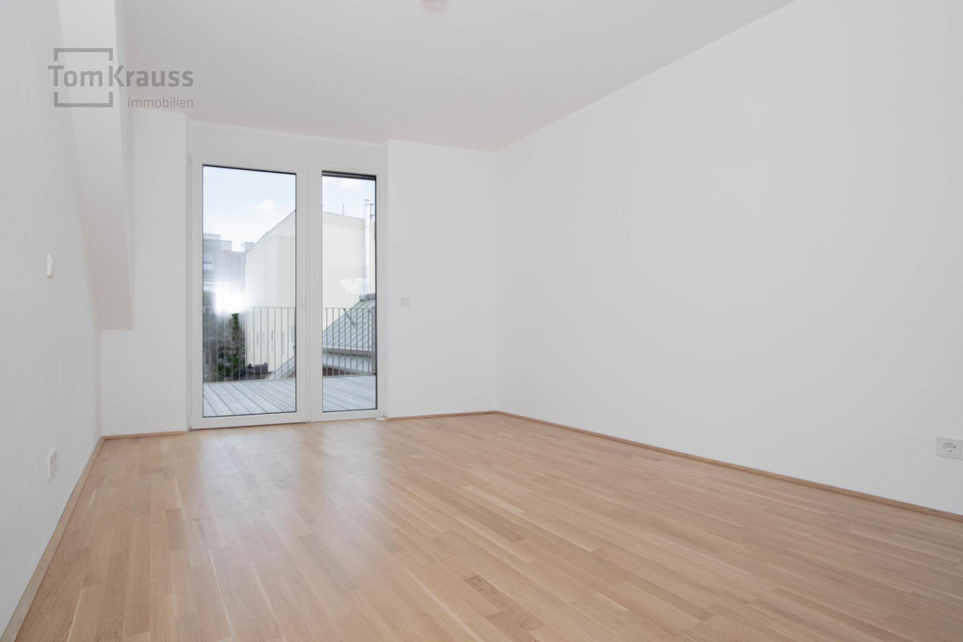 Heller Raum mit Holzboden, weißen Wänden und Zugang zu einem kleinen Balkon.