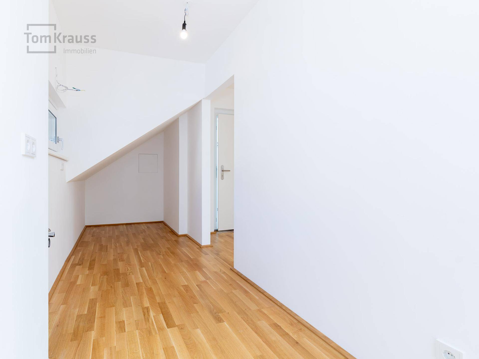 Leerer Küchenbereich mit Holzboden und Dachschräge, bereit für die Installation einer Einbauküche.