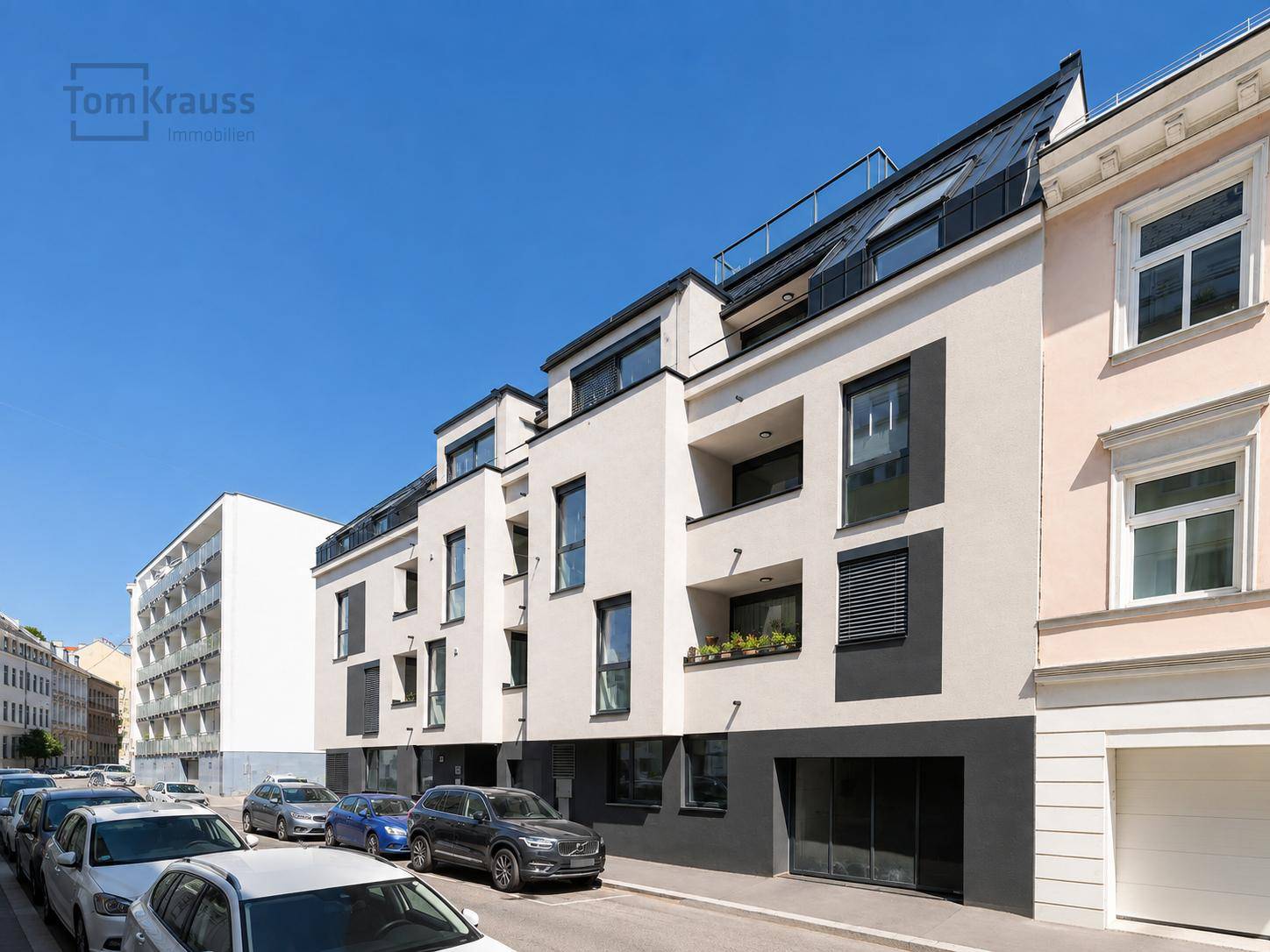 Neubau mit moderner Architektur, heller Fassade und Balkonen in einer städtischen Straße.