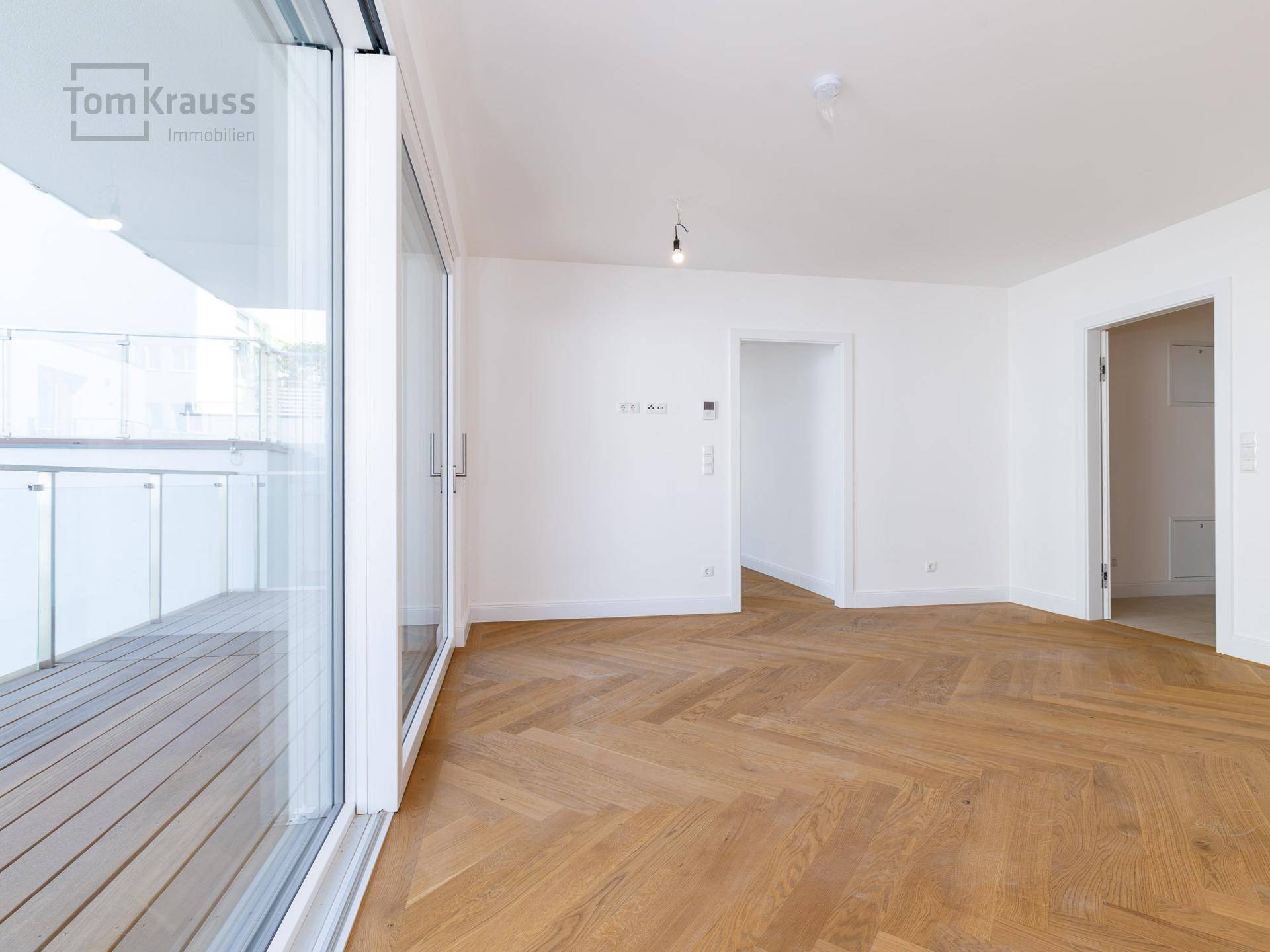 Heller Raum mit Fischgrätparkett und großen Schiebetüren zum Balkon.