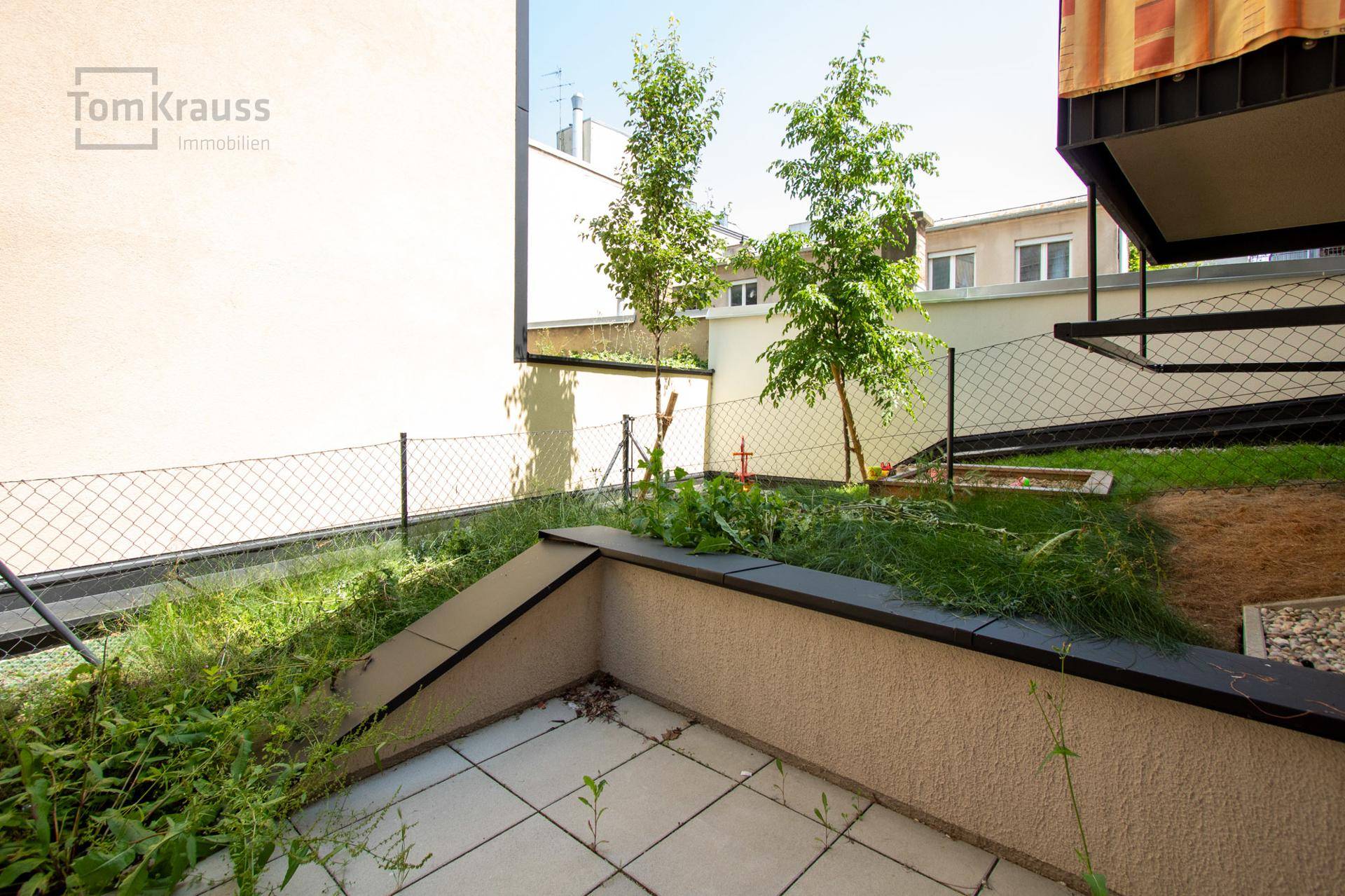 Unmöblierte Terrasse mit Fliesenboden und angrenzender Grünfläche, bereit zur Gestaltung.