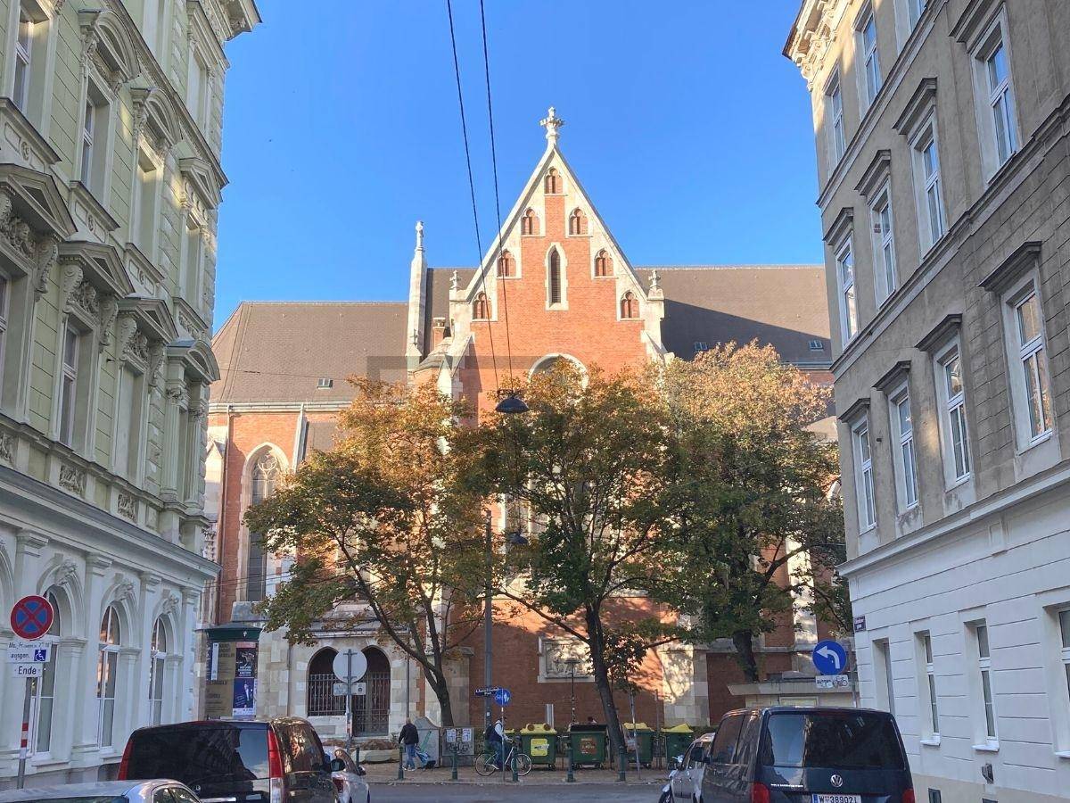 Straßenansicht mit historischen Gebäuden und einer Kirche im Hintergrund unter blauem Himmel.