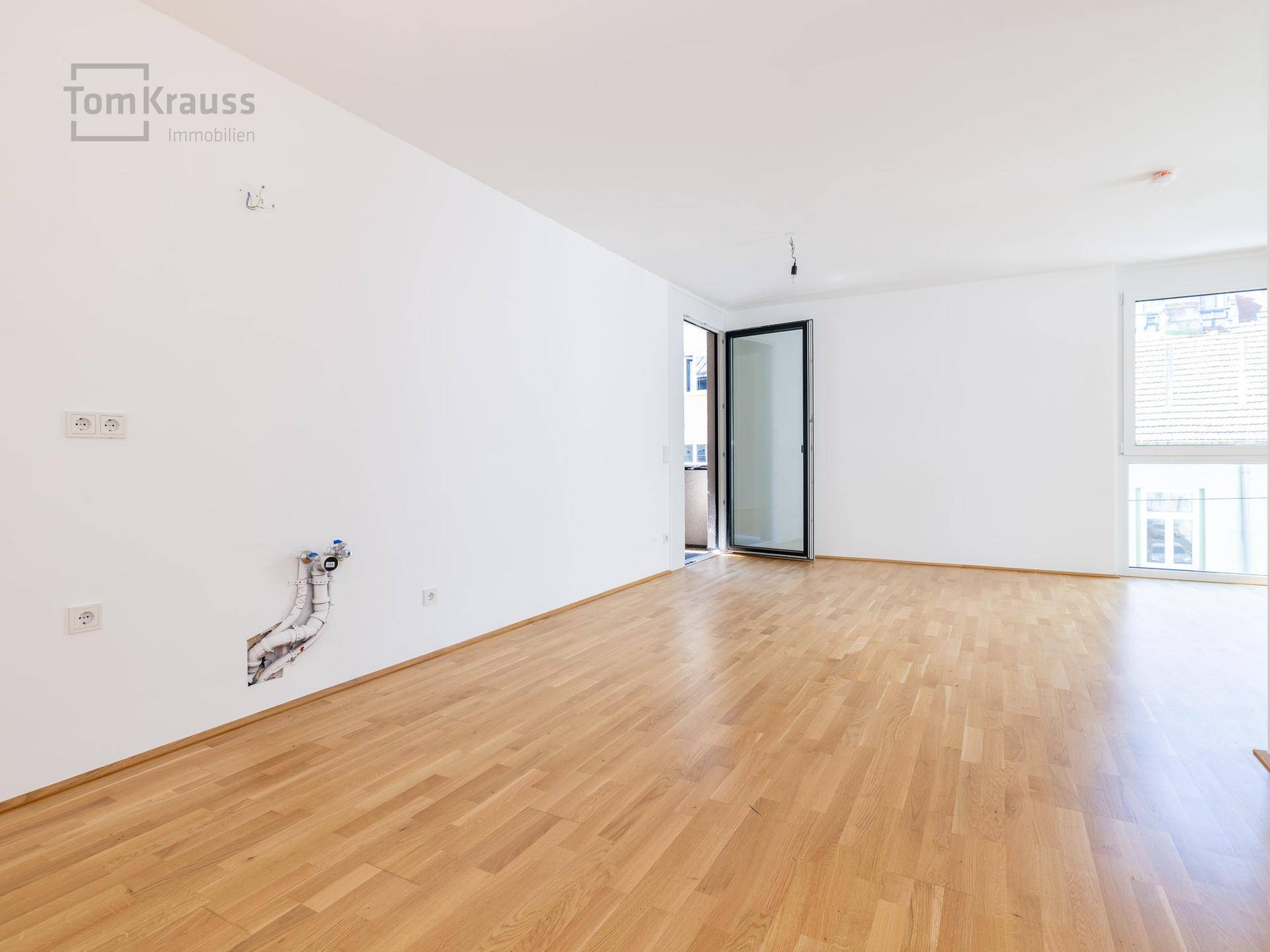 Leerer Raum mit Parkettboden und Zugang zum Außenbereich, vorbereitet für Kücheninstallationen.