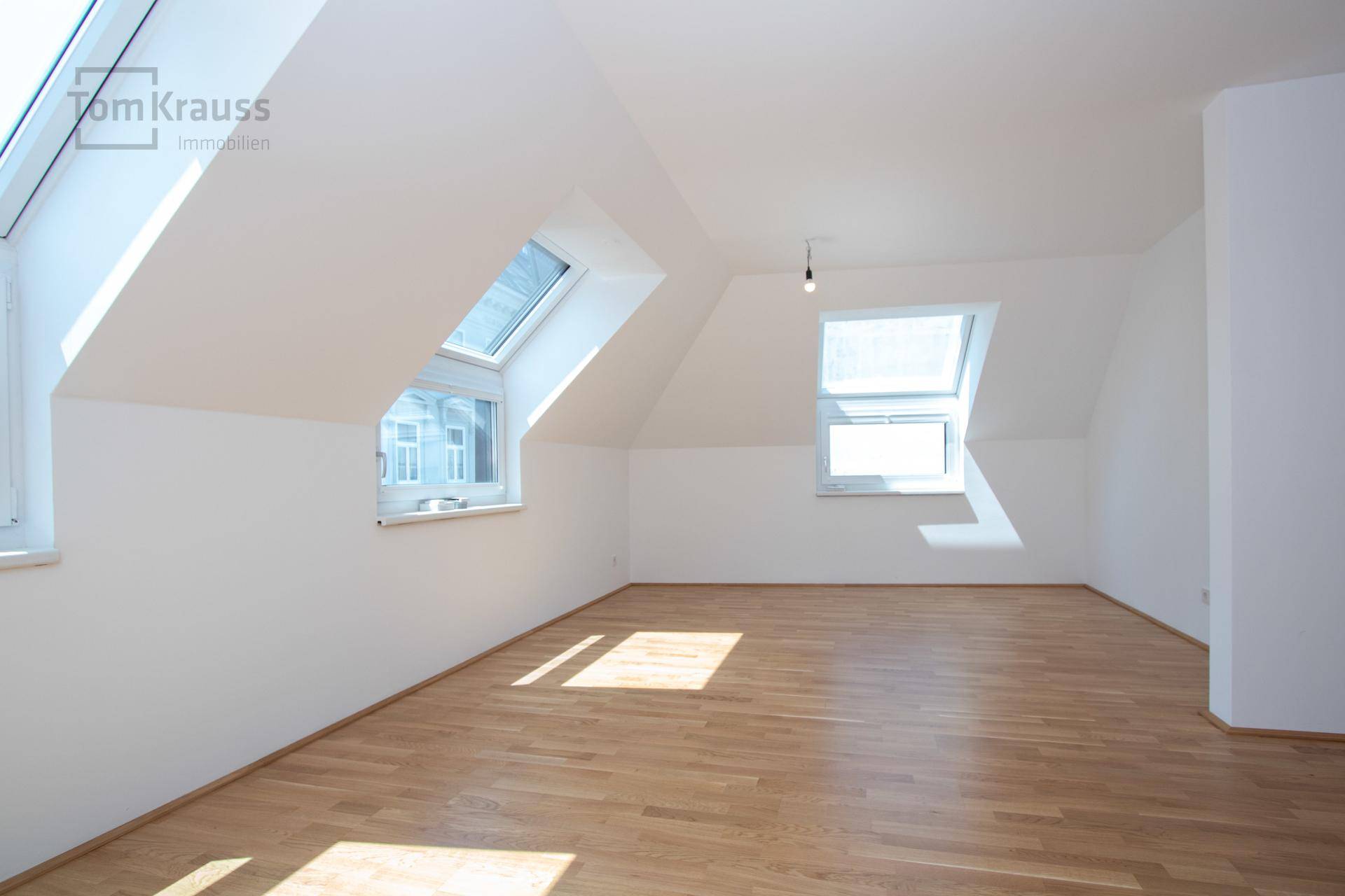 Geräumiges, leeres Wohnzimmer im Dachgeschoss mit Holzparkett und mehreren Dachfenstern.