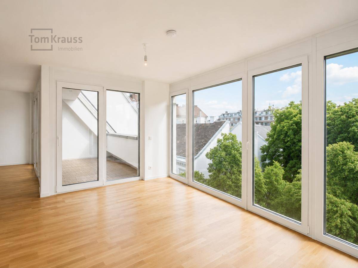 Heller, leerer Raum mit großen Fenstern, Holzboden und Zugang zu einem kleinen Balkon.