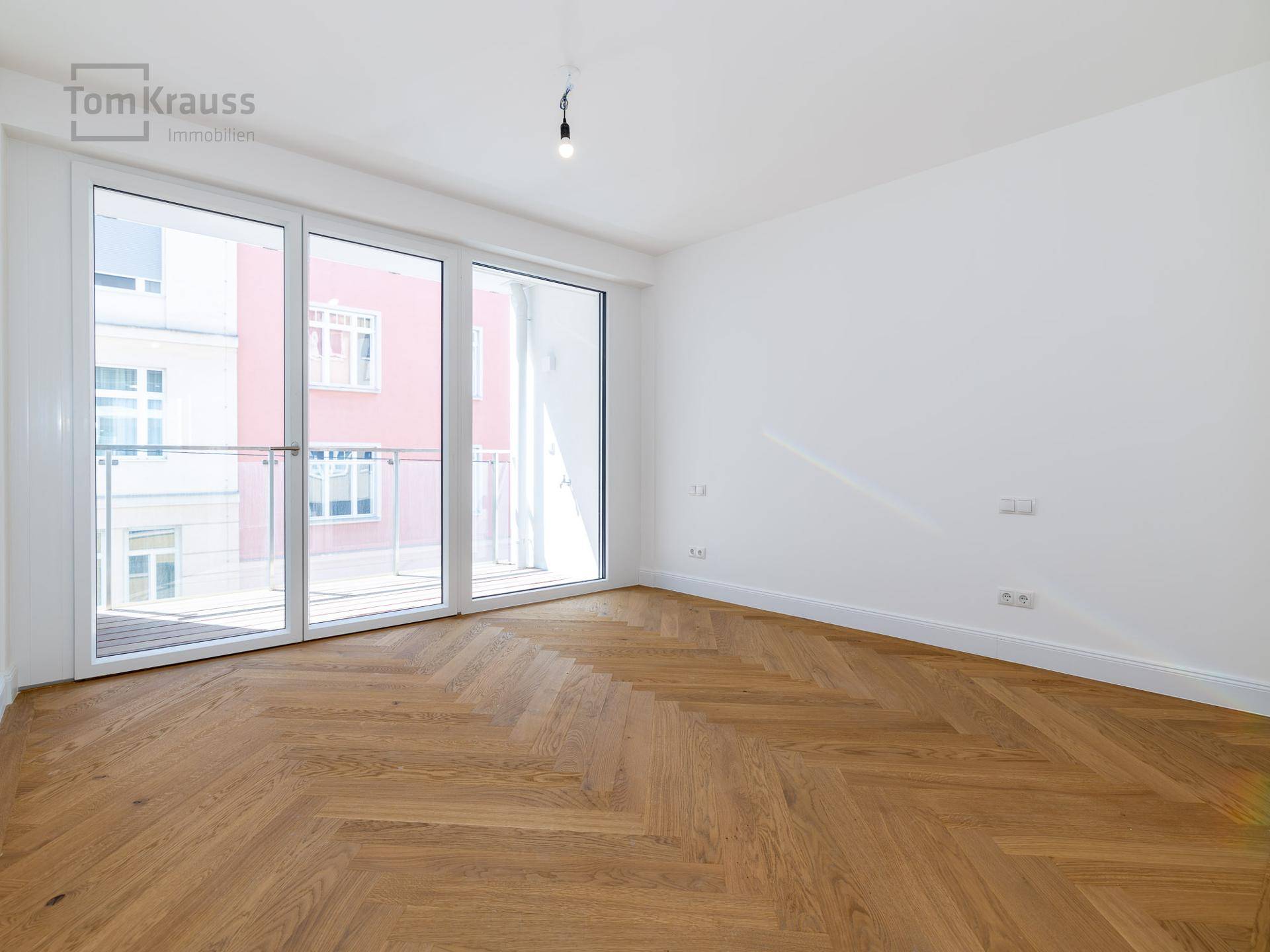 Lichtdurchflutetes Zimmer mit Fischgrätparkett und bodentiefen Fenstern, die viel Tageslicht hereinlassen.