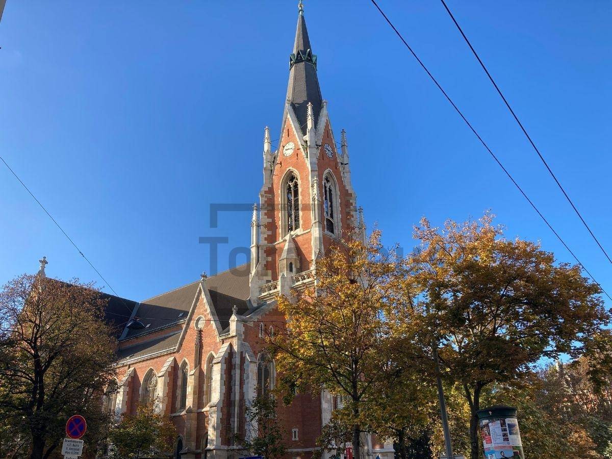 Gotische Kirche mit hohem Turm und detaillierter Architektur, umgeben von Herbstbäumen.