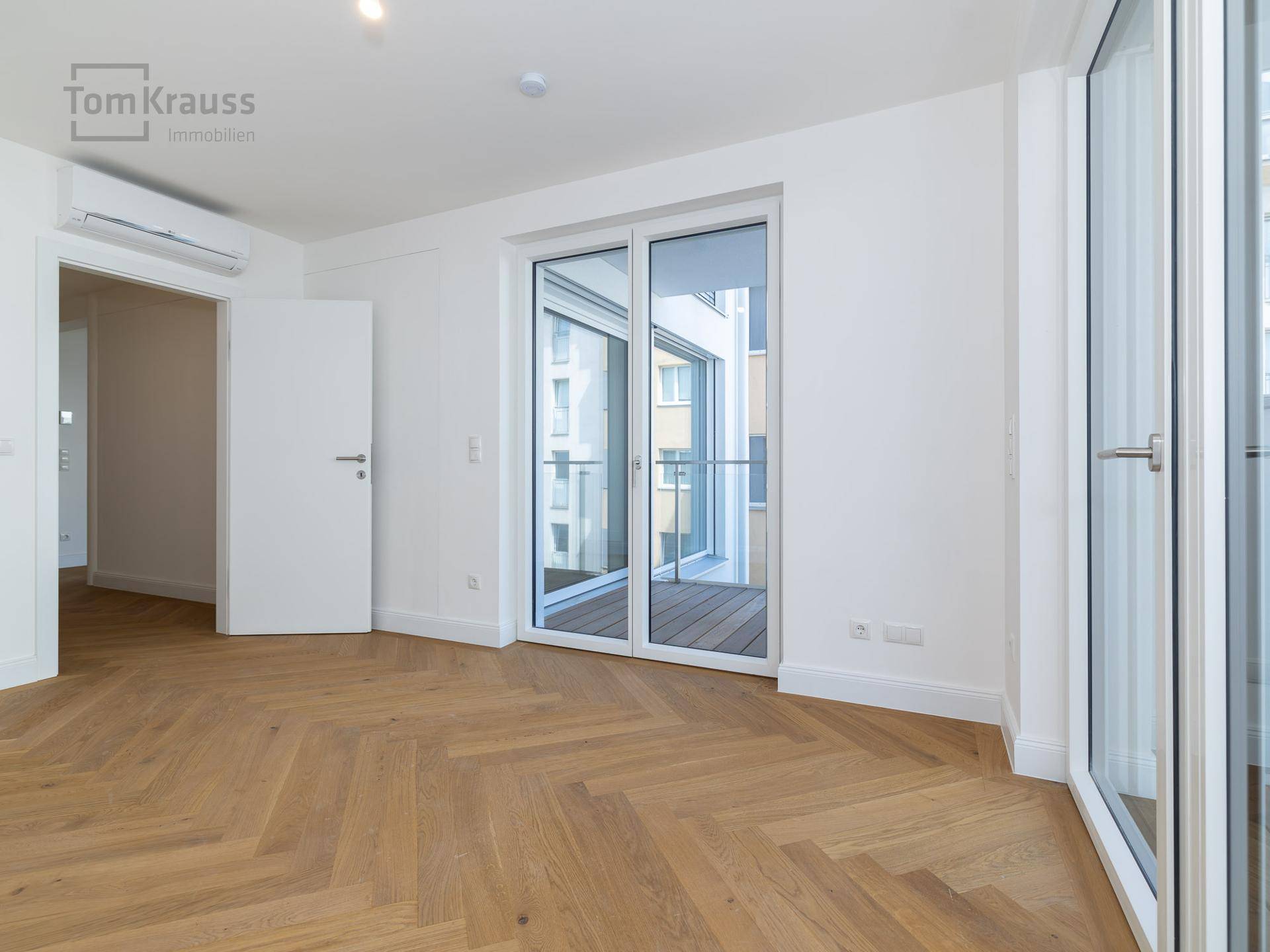 Geräumiges Zimmer mit Fischgrätparkett, Klimaanlage und Zugang zu einem Balkon.