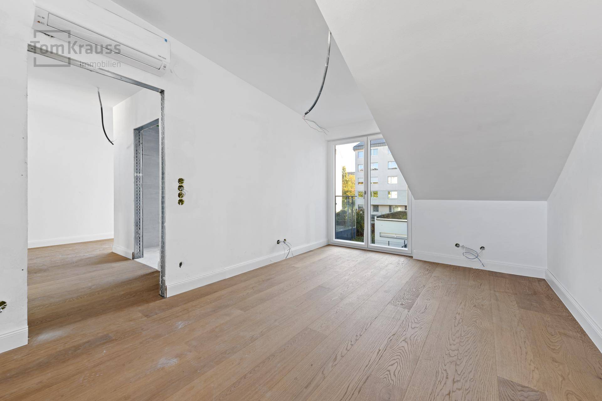 Leeres Schlafzimmer mit Holzboden, Dachschräge und Schiebetür zu einem kleinen Balkon.