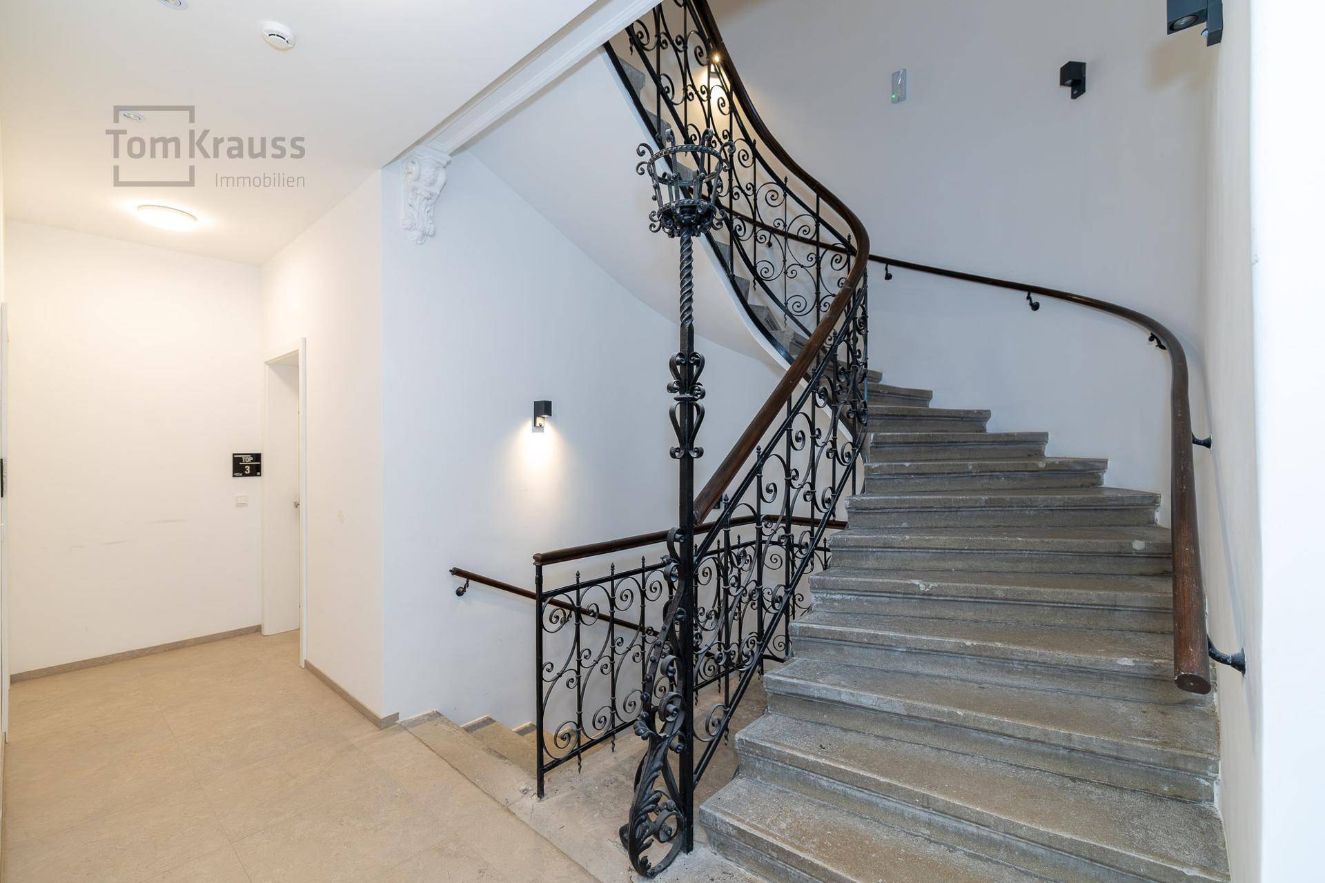 Historisches Treppenhaus mit schmiedeeisernem Geländer und Steinstufen in einem Altbau.