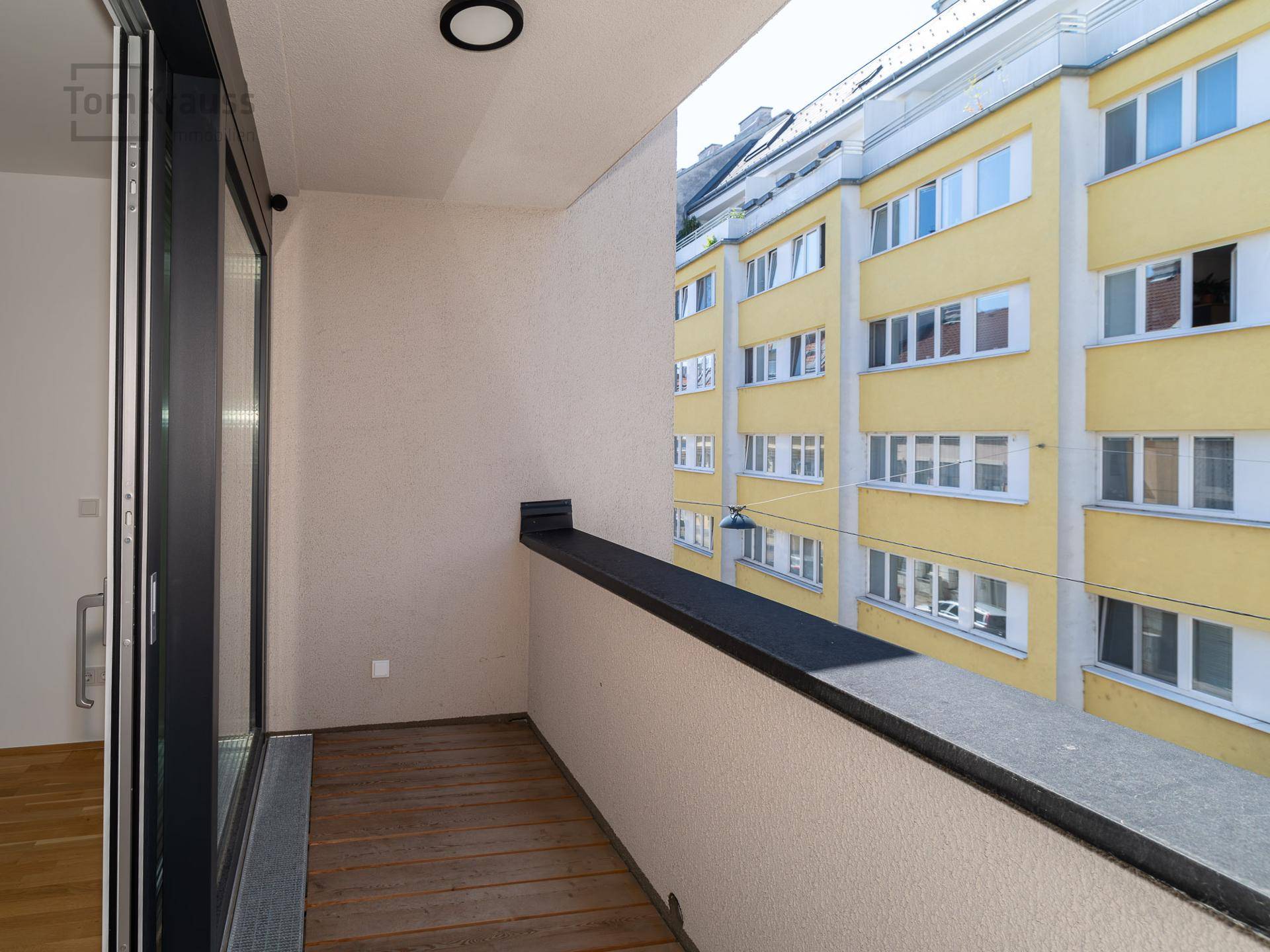 Leerer Balkon mit Holzboden und Schiebetüren, bietet einen Blick auf die umliegenden Gebäude.