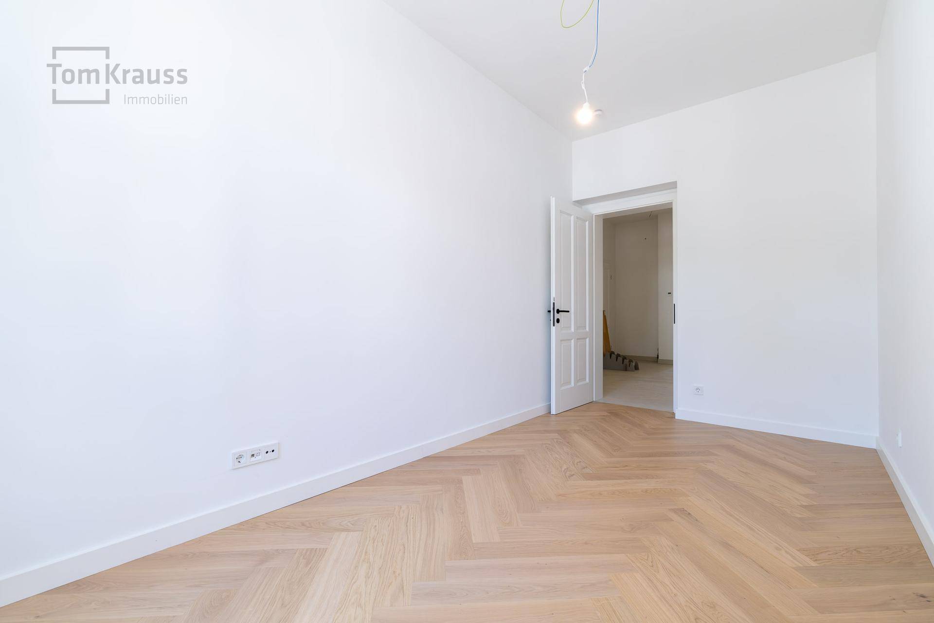 Heller, leerer Raum mit Fischgrätparkett und Türöffnung, ideal als Schlafzimmer.