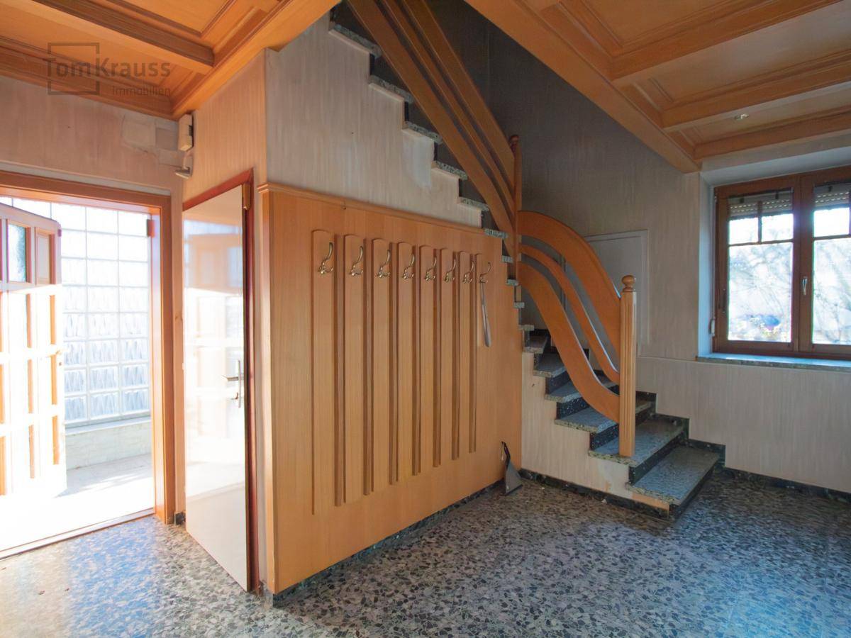 Eingangsbereich mit Holzdecke, dunklem Terrazzoboden und einer geschwungenen Holztreppe.