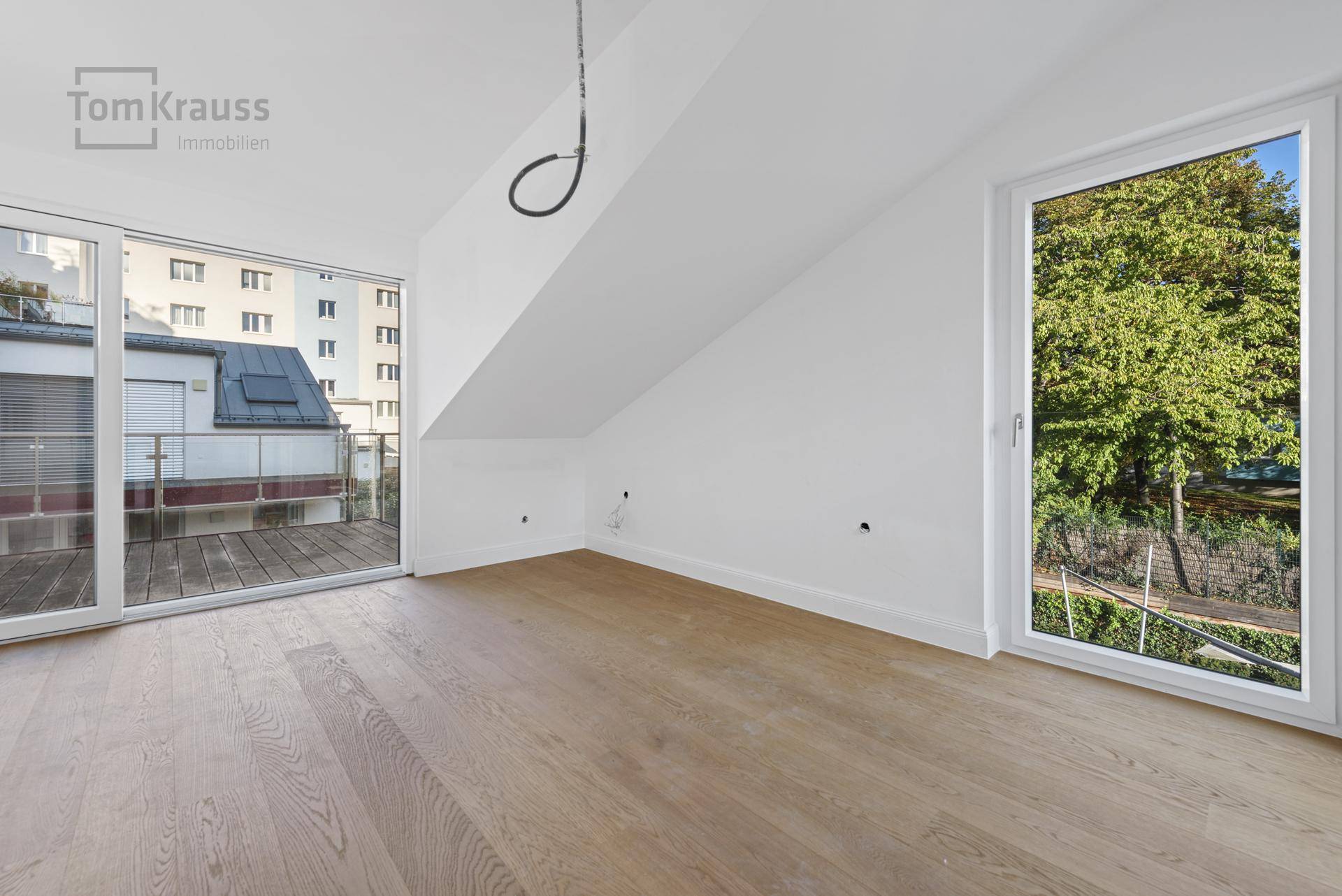 Heller Raum mit Holzboden, Dachschräge und Zugang zu einem Balkon mit Blick ins Grüne.