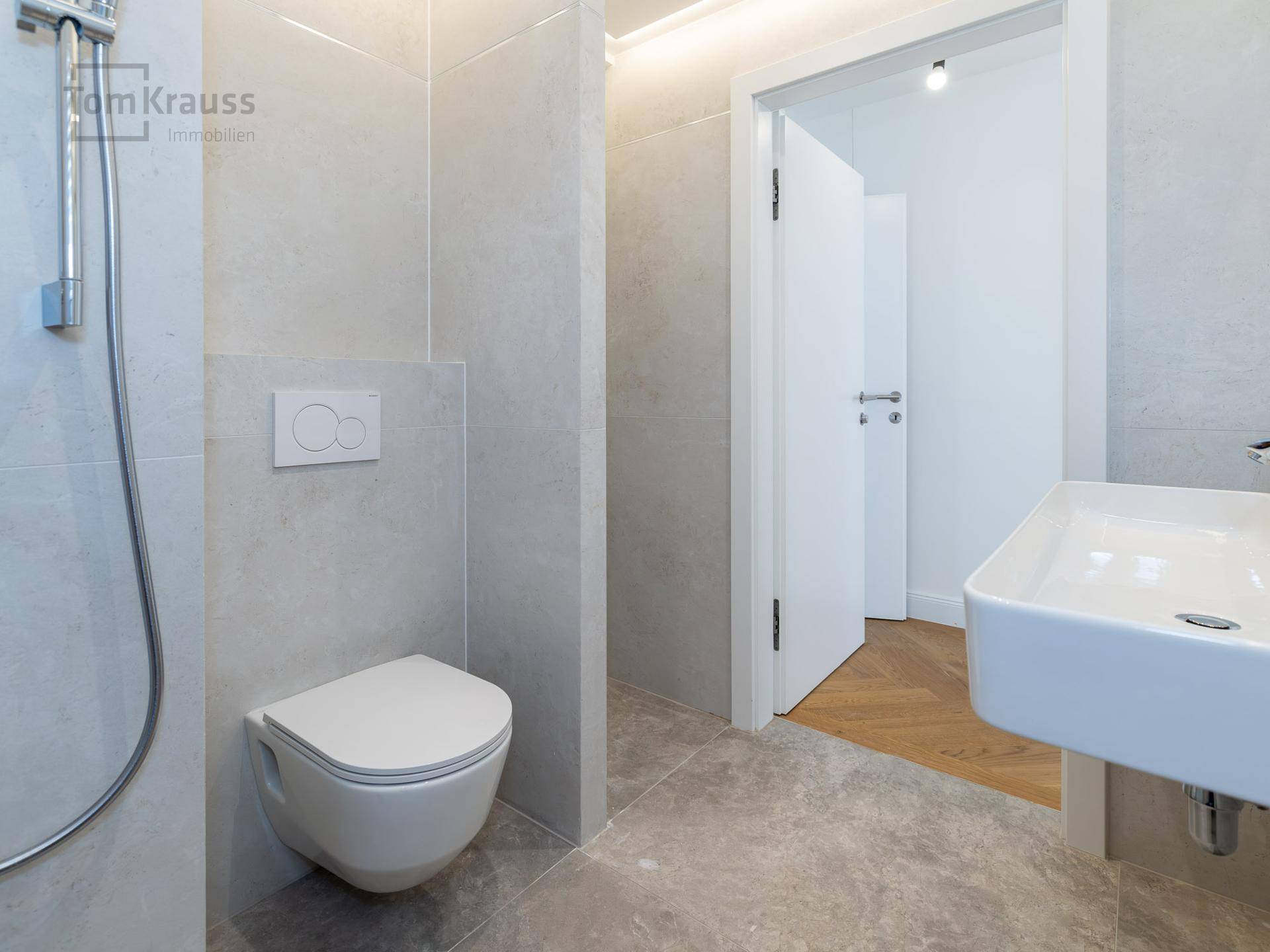 Modernes Badezimmer mit Wand-WC, Waschbecken und Dusche, in hellen Grautönen gehalten.