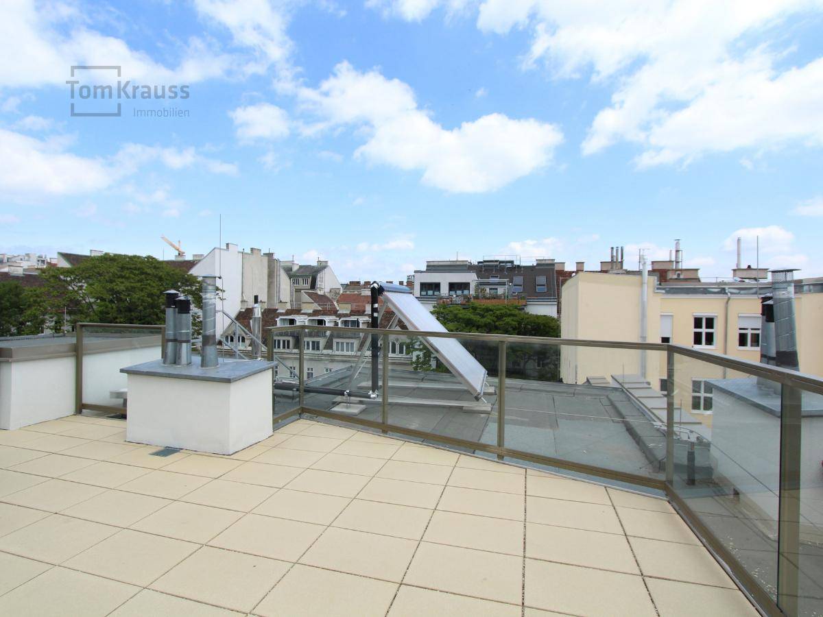 Weitläufige Dachterrasse mit hellen Fliesen, Glasgeländer und Panoramablick über die Stadt.