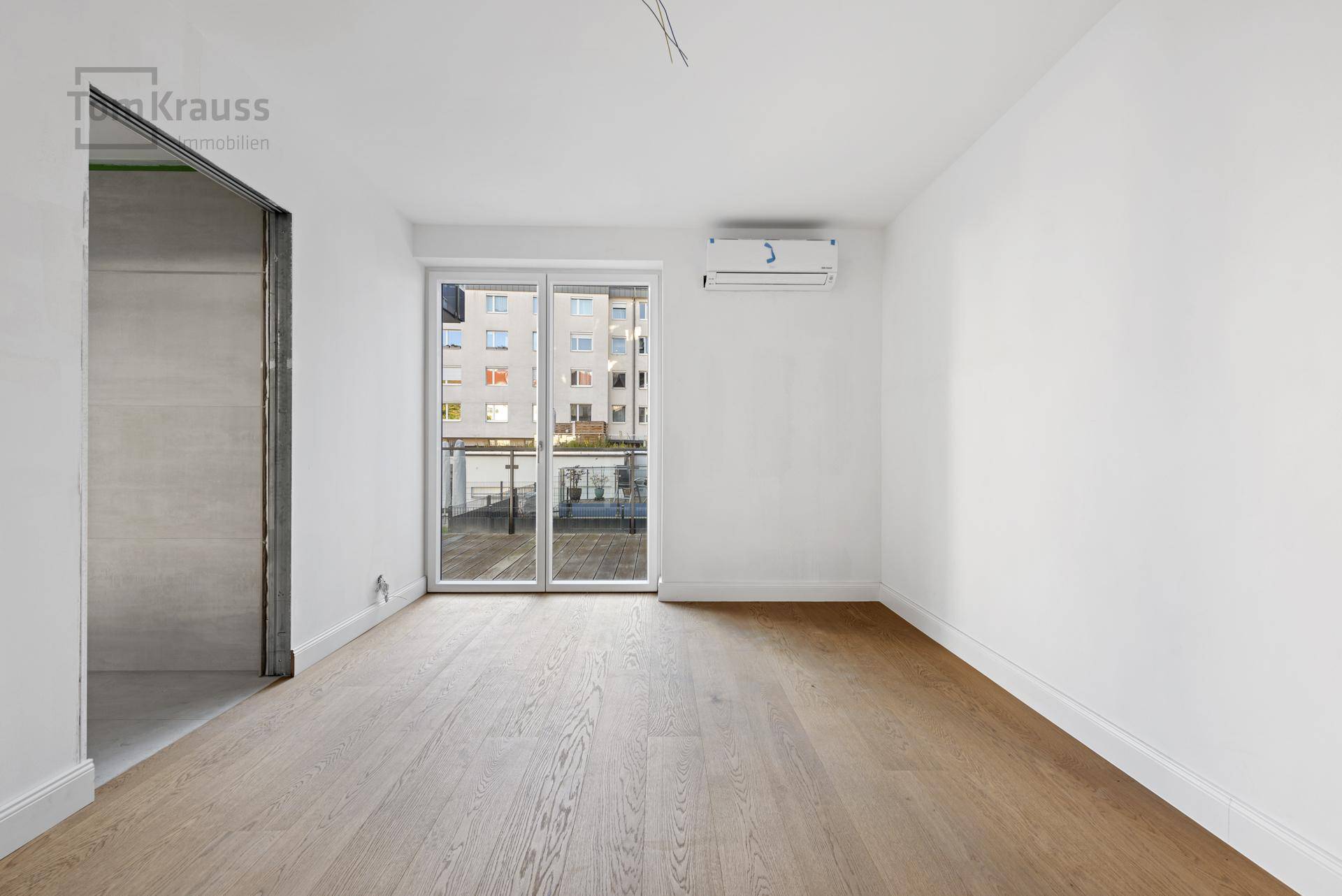 Leeres Schlafzimmer mit Holzboden, Klimaanlage und Zugang zu einem kleinen Balkon.
