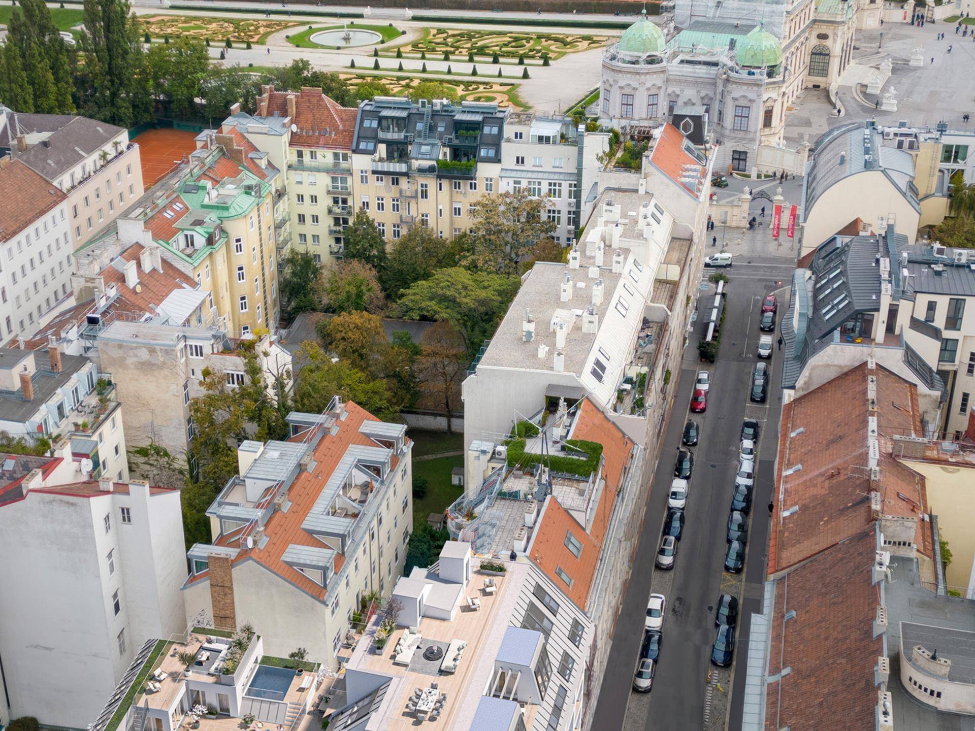Luftaufnahme eines Stadtviertels mit Gebäuden, Dachterrassen und einem Park im Hintergrund.