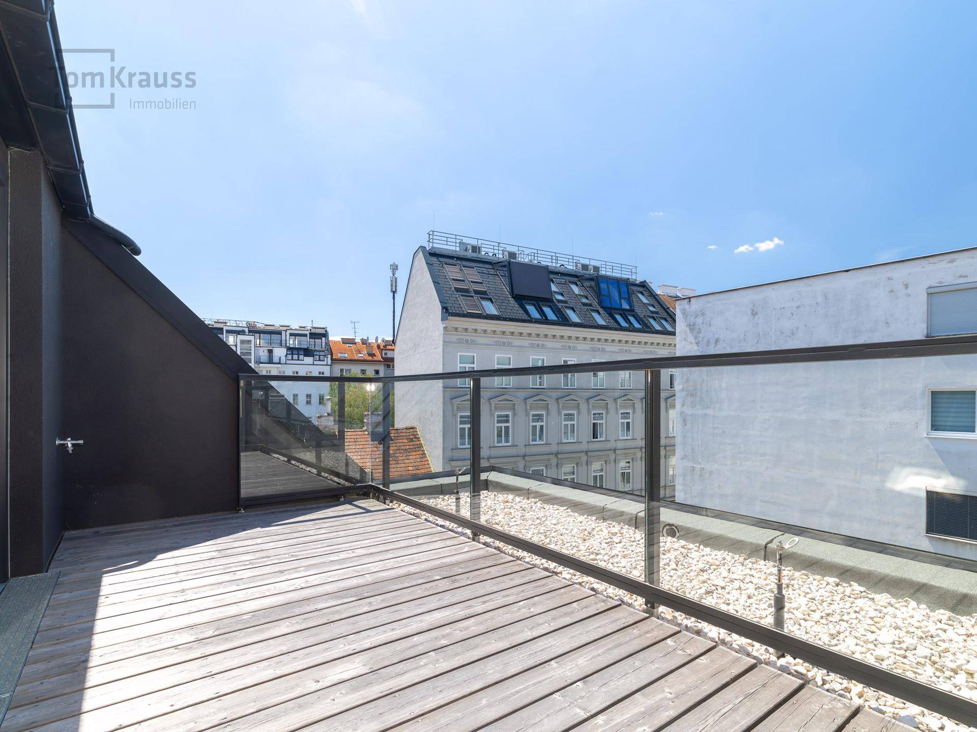 Geräumige Dachterrasse mit Holzboden und Glasgeländer, bietet einen weiten Blick über die Stadt.