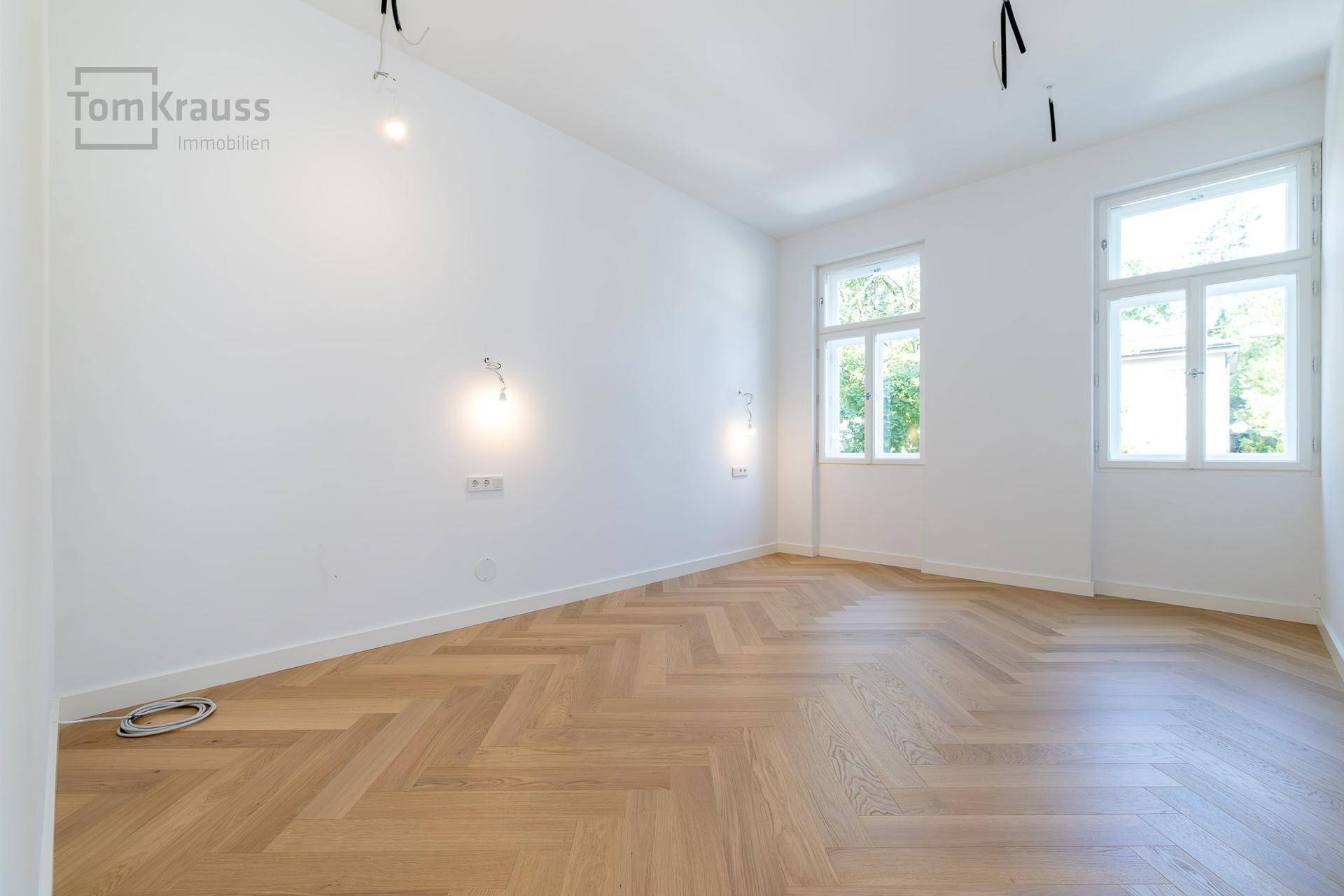 Heller, leerer Raum mit Fischgrätparkett und zwei Fenstern, ideal als Schlafzimmer.