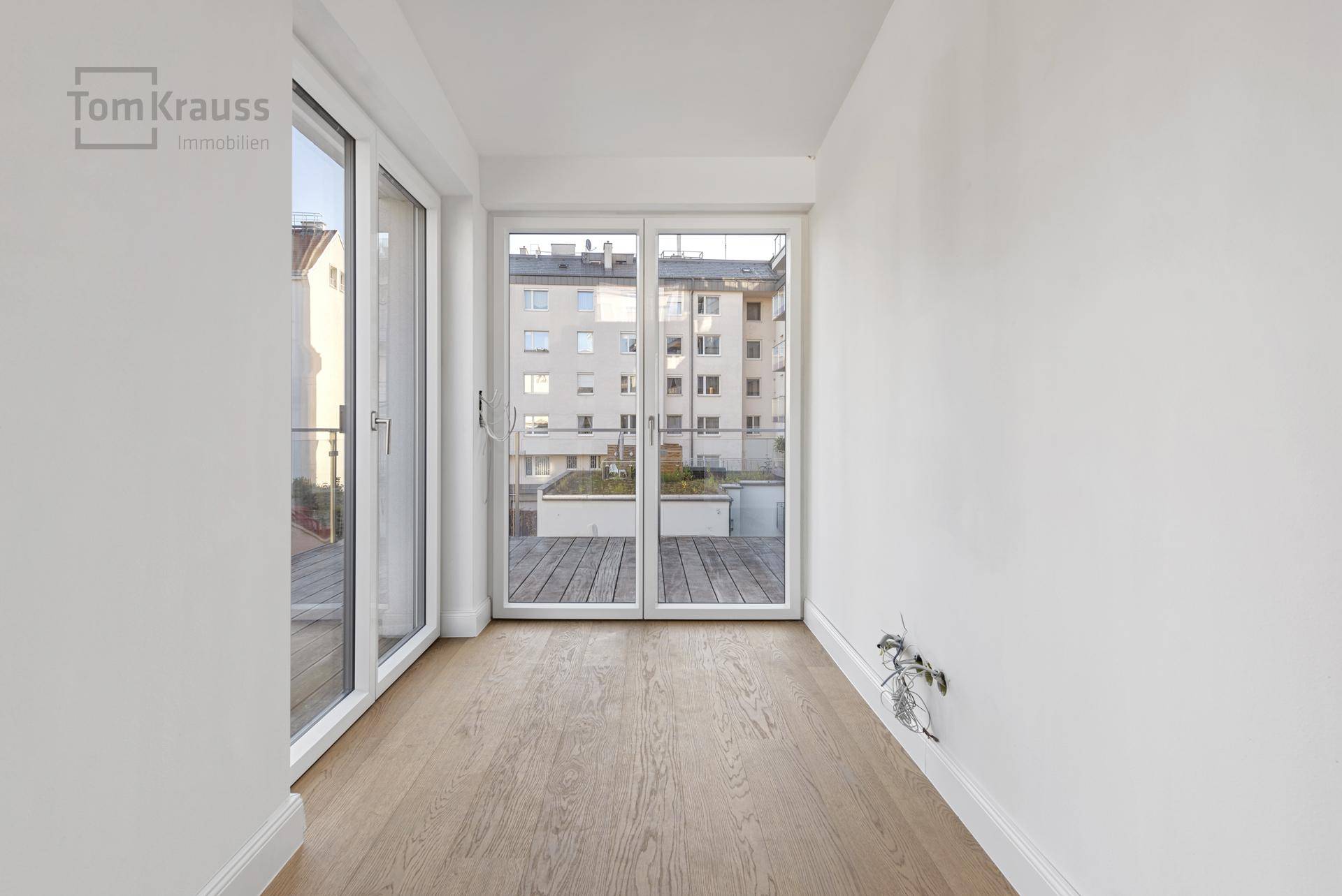 Heller, leerer Raum mit Holzboden und französischen Balkonen, ideal als Schlaf- oder Ankleidezimmer.