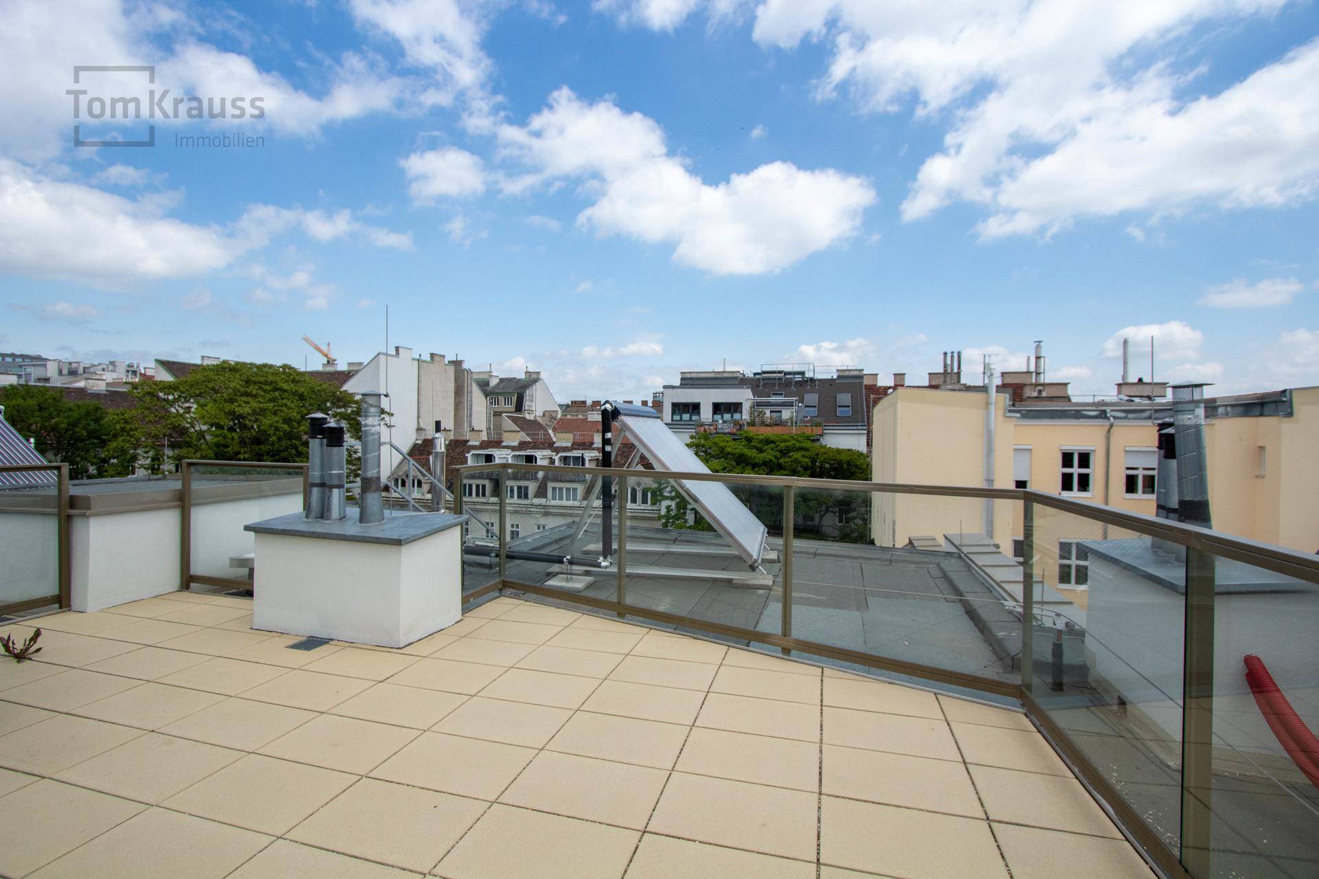 Weitläufige Dachterrasse mit hellen Fliesen, Glasgeländer und Panoramablick über die Stadt.