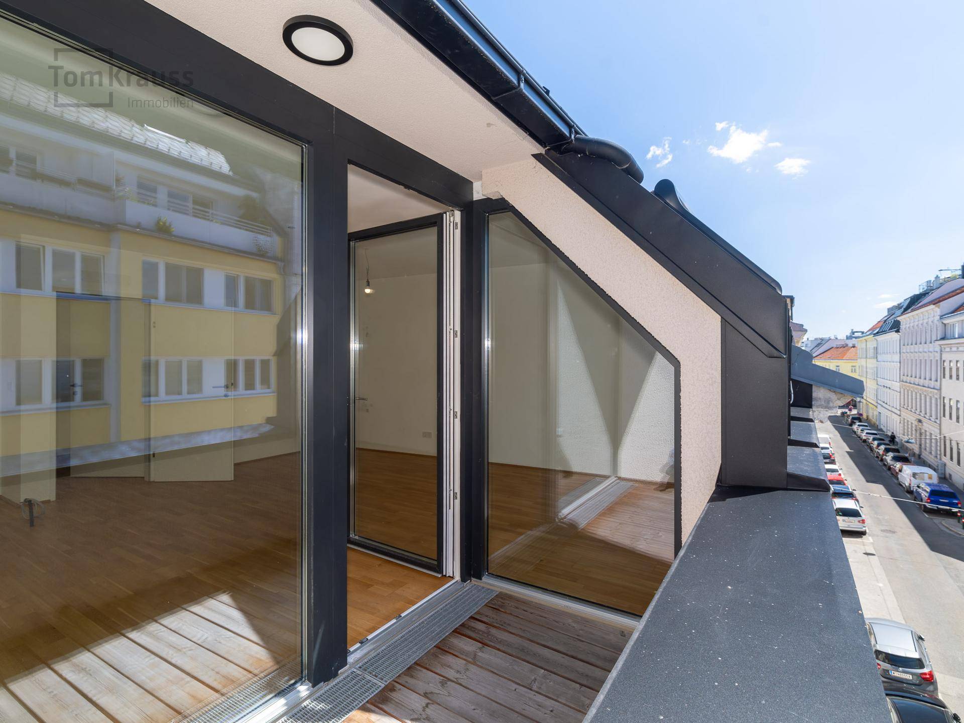 Unmöblierter Balkon mit Holzboden und Blick auf die Straße und angrenzende Gebäude.