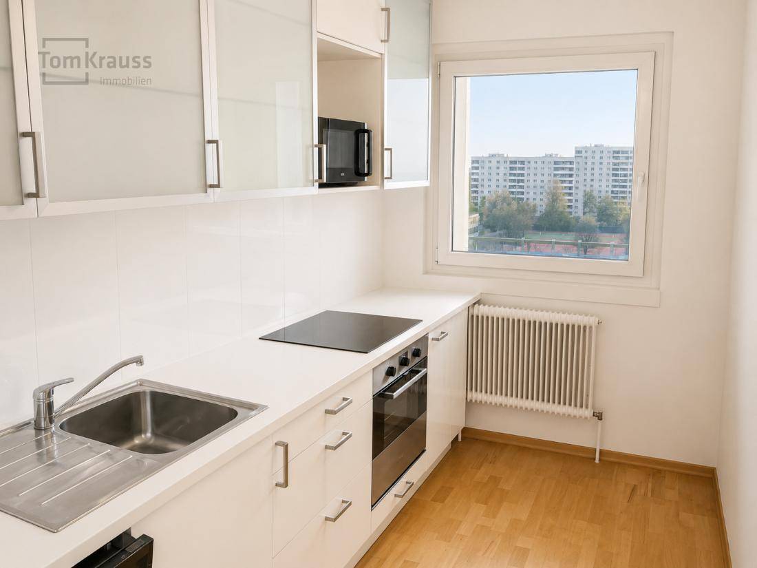 Helle Einbauküche mit weißen Schränken, Kochfeld und Fenster mit Stadtblick.