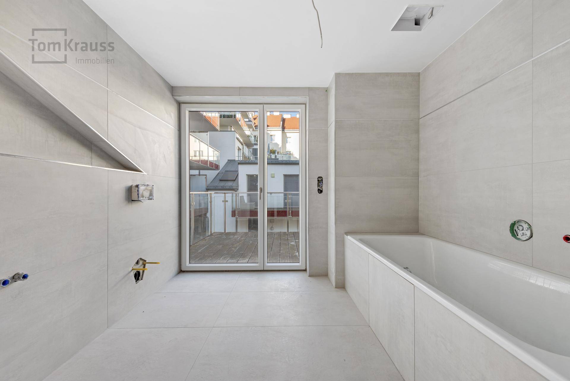 Leeres Badezimmer mit Badewanne, Duschbereich und Fliesenboden, bereit für die Endmontage.
