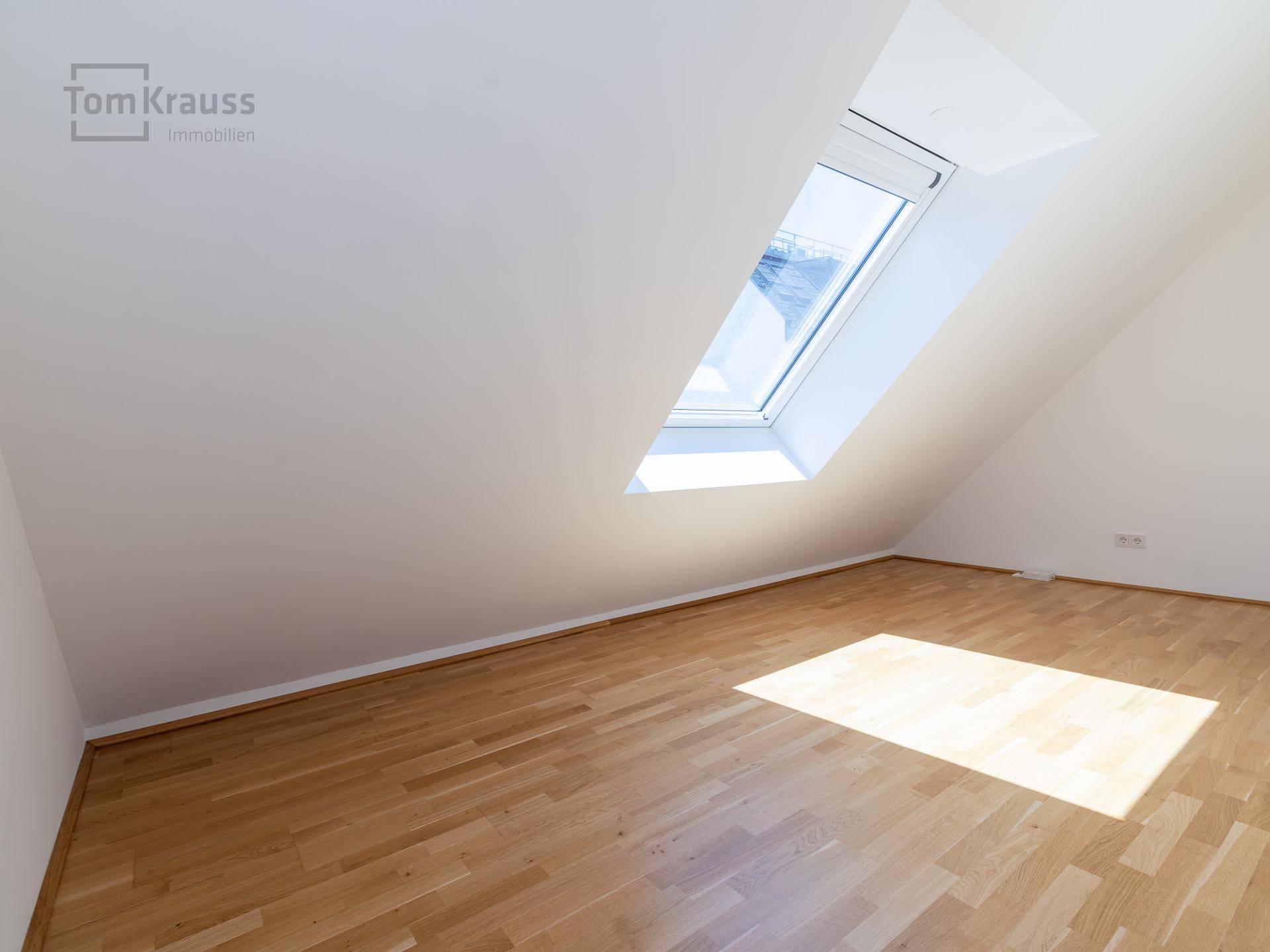 Leeres Kinderzimmer mit Holzboden und großem Dachfenster, bietet viel natürliches Licht.