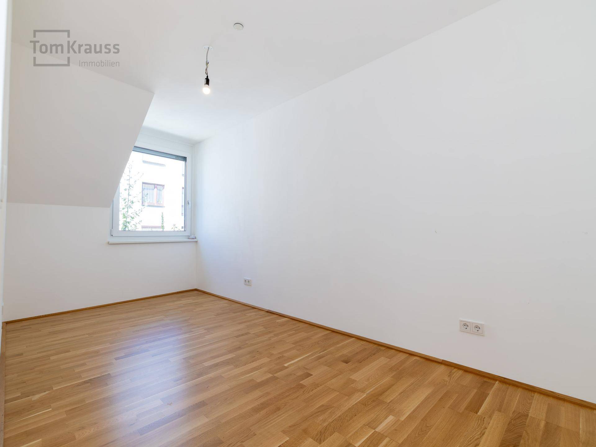 Leeres Zimmer mit Holzparkettboden und einem Fenster, ideal als Büro oder Gästezimmer.