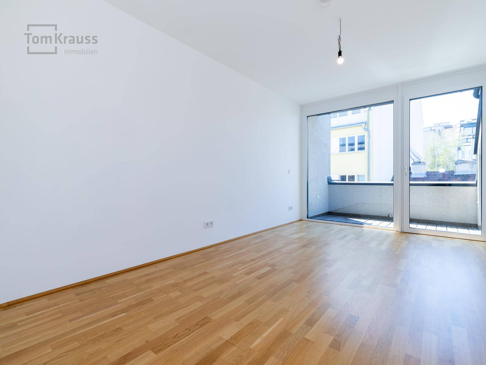 Leeres Schlafzimmer mit Holzparkettboden und großen Fenstern, die Zugang zum Balkon bieten.