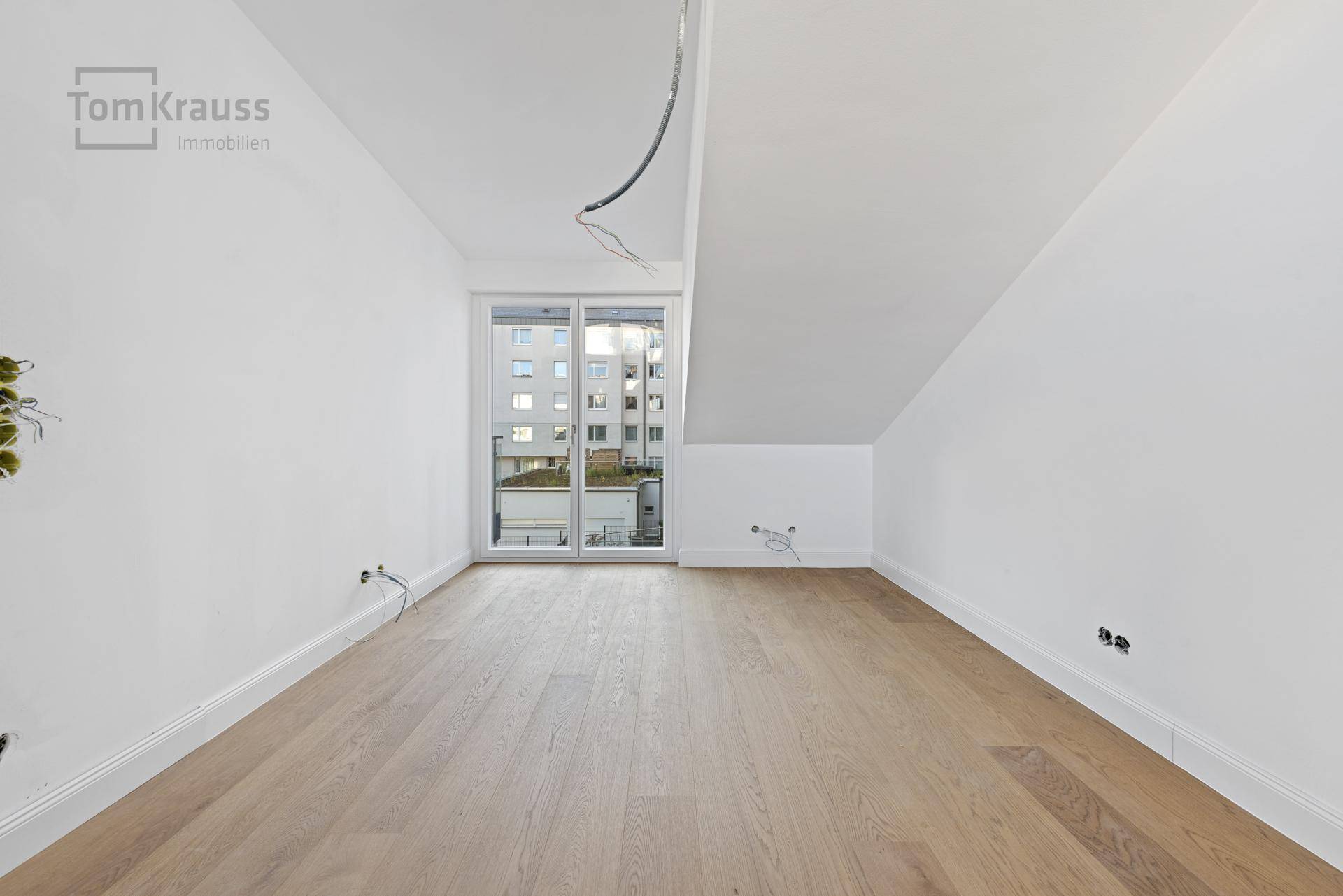 Leeres Schlafzimmer mit Holzboden, Dachschräge und französischem Balkon, bereit zum Einrichten.