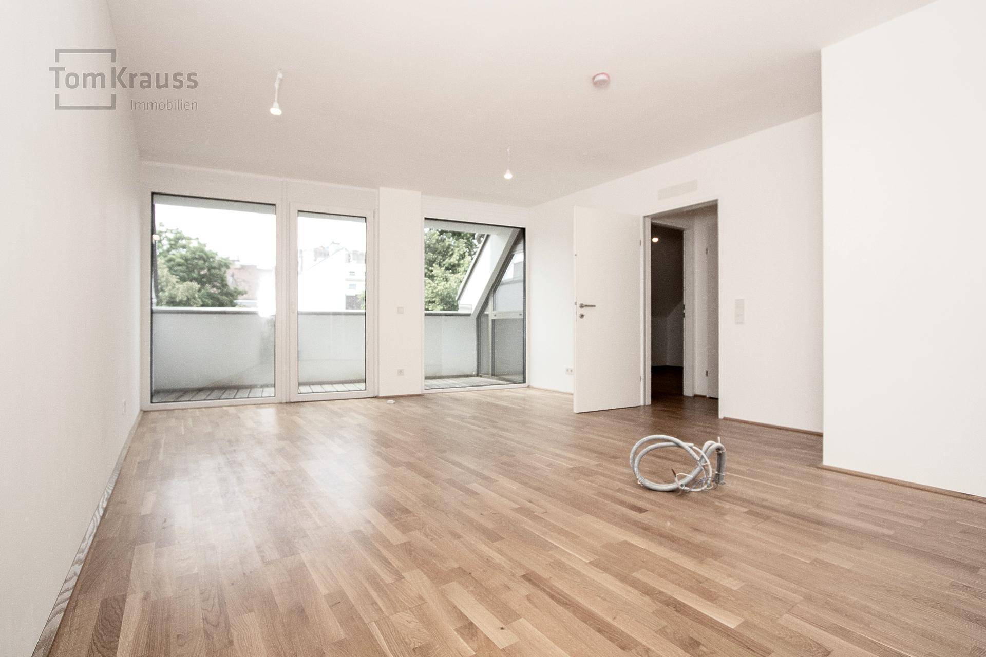 Helles, leeres Zimmer mit Parkettboden und zwei Zugängen zu Balkonen.