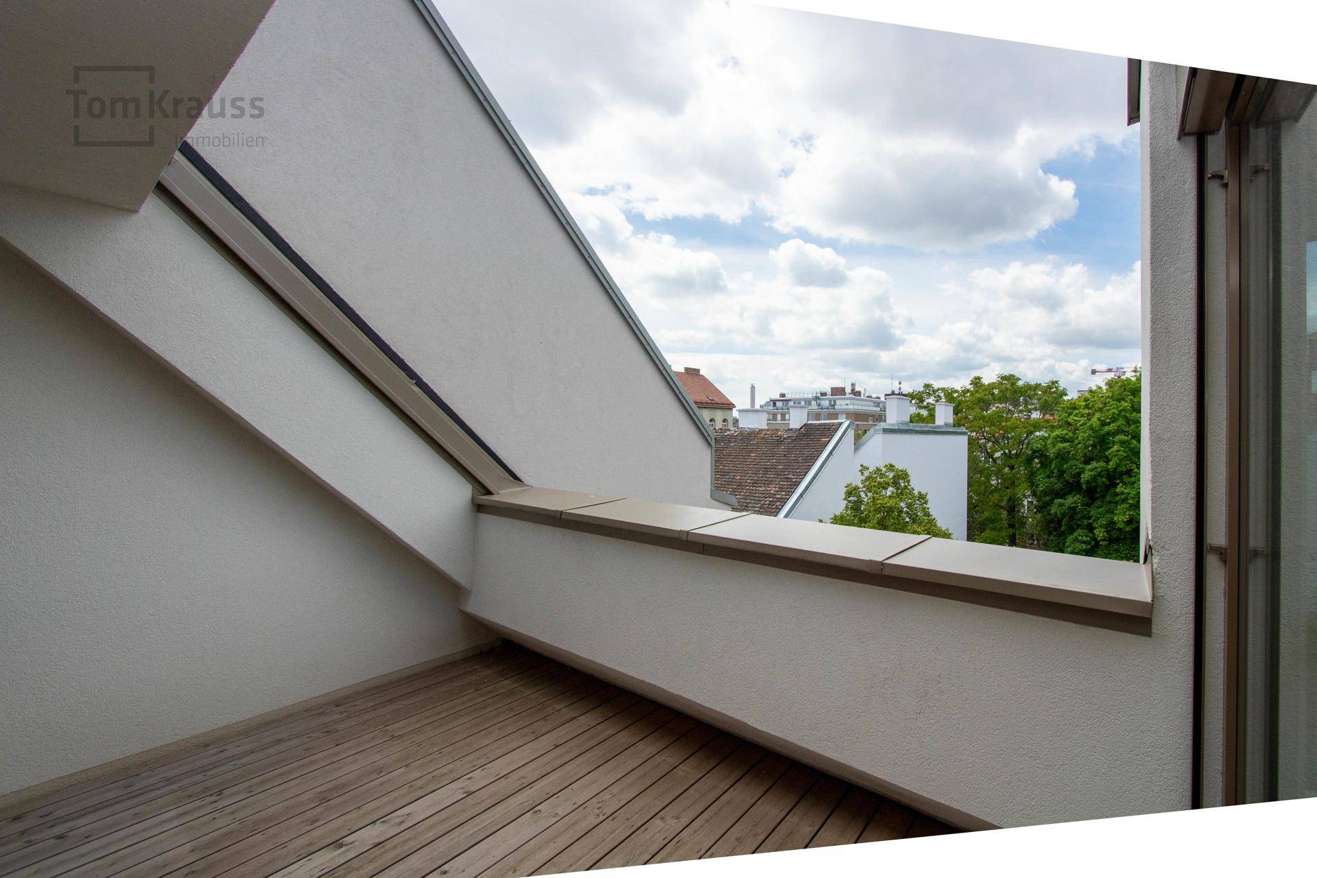 Überdachte Loggia mit Holzdeck und Blick auf die umliegenden Dächer und den Himmel.