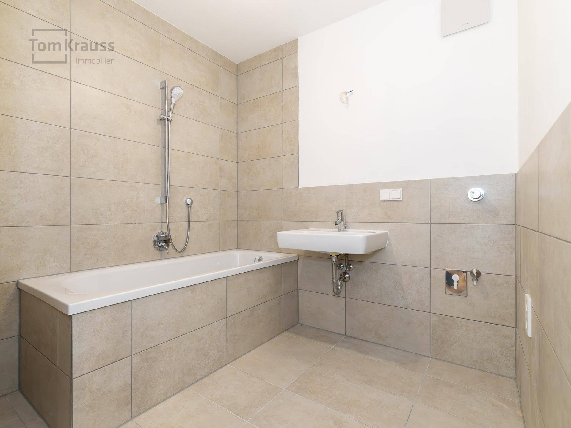 Modernes Badezimmer mit beigefarbenen Fliesen, Badewanne mit Duschfunktion und einem Waschbecken.