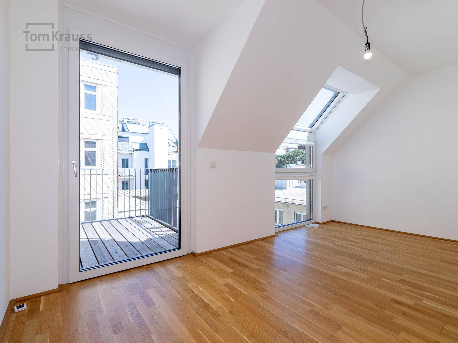 Unmöbliertes Schlafzimmer mit Holzboden, Dachschrägen und Zugang zu einem Balkon.