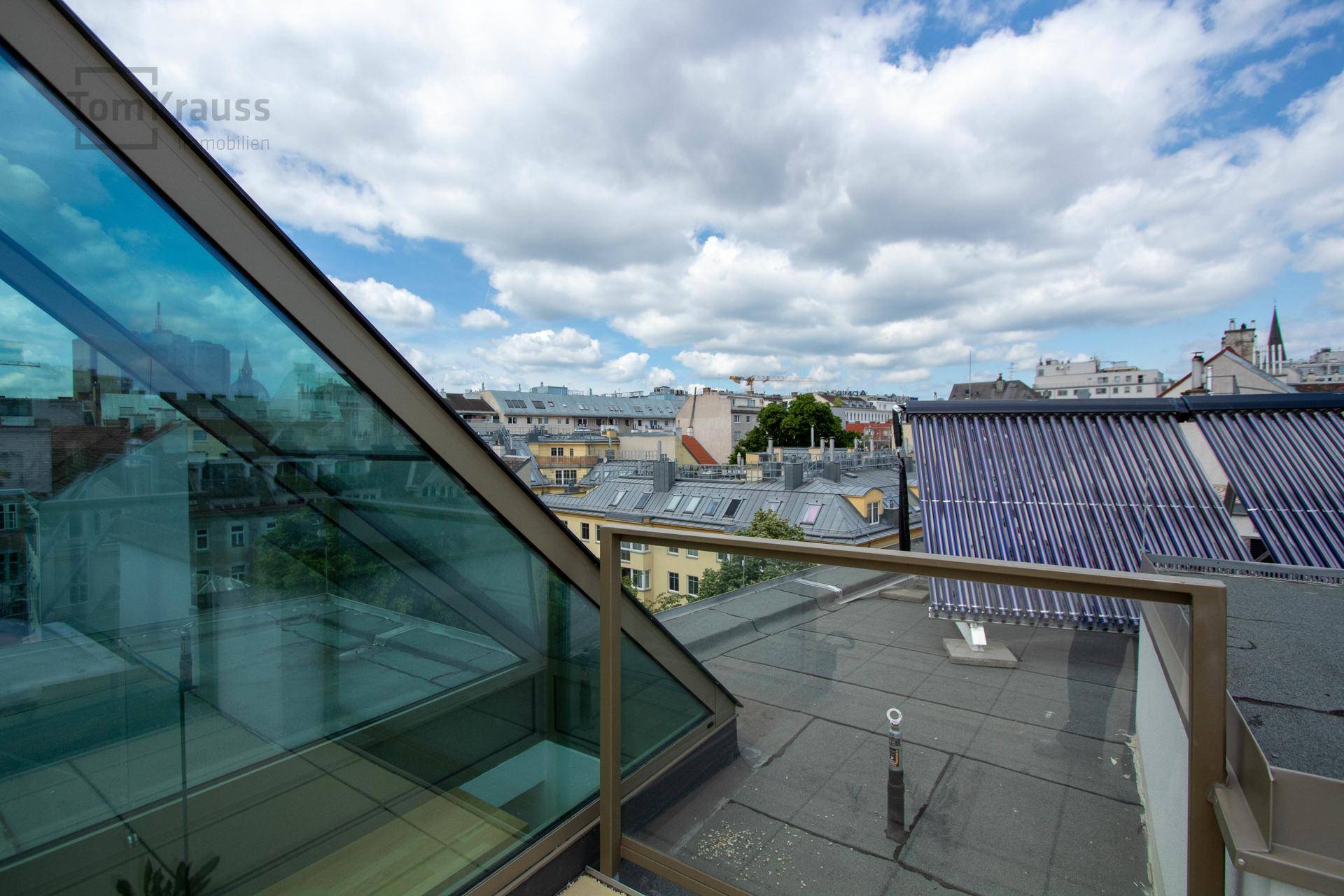 Blick von oben über die Dächer der Stadt mit einer modernen Glasstruktur im Vordergrund.